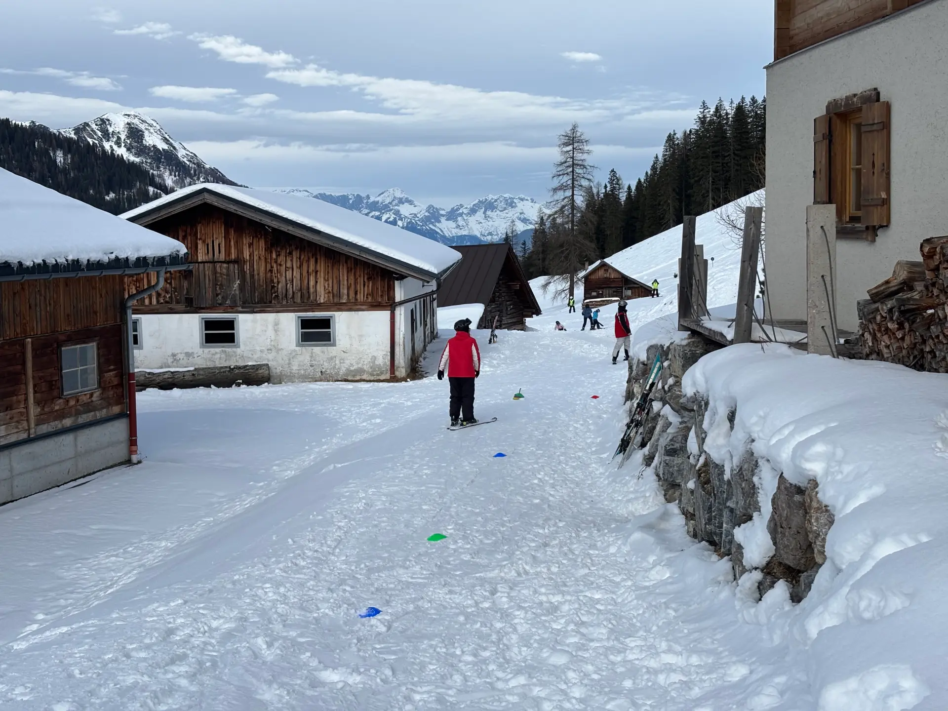 Neben einer Skihütte ist auf dem Schnee ein einfacher Slalomparcour aufgebaut, den ein Schüler mit Skiern durchläuft. 
