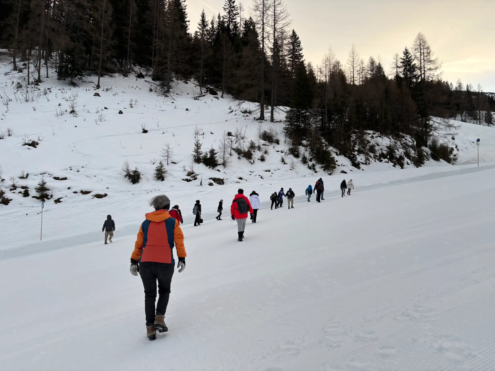 Eine Hand voll Menschen in Winterkleidung läuft eine flache, schneebedeckte Piste nach oben.