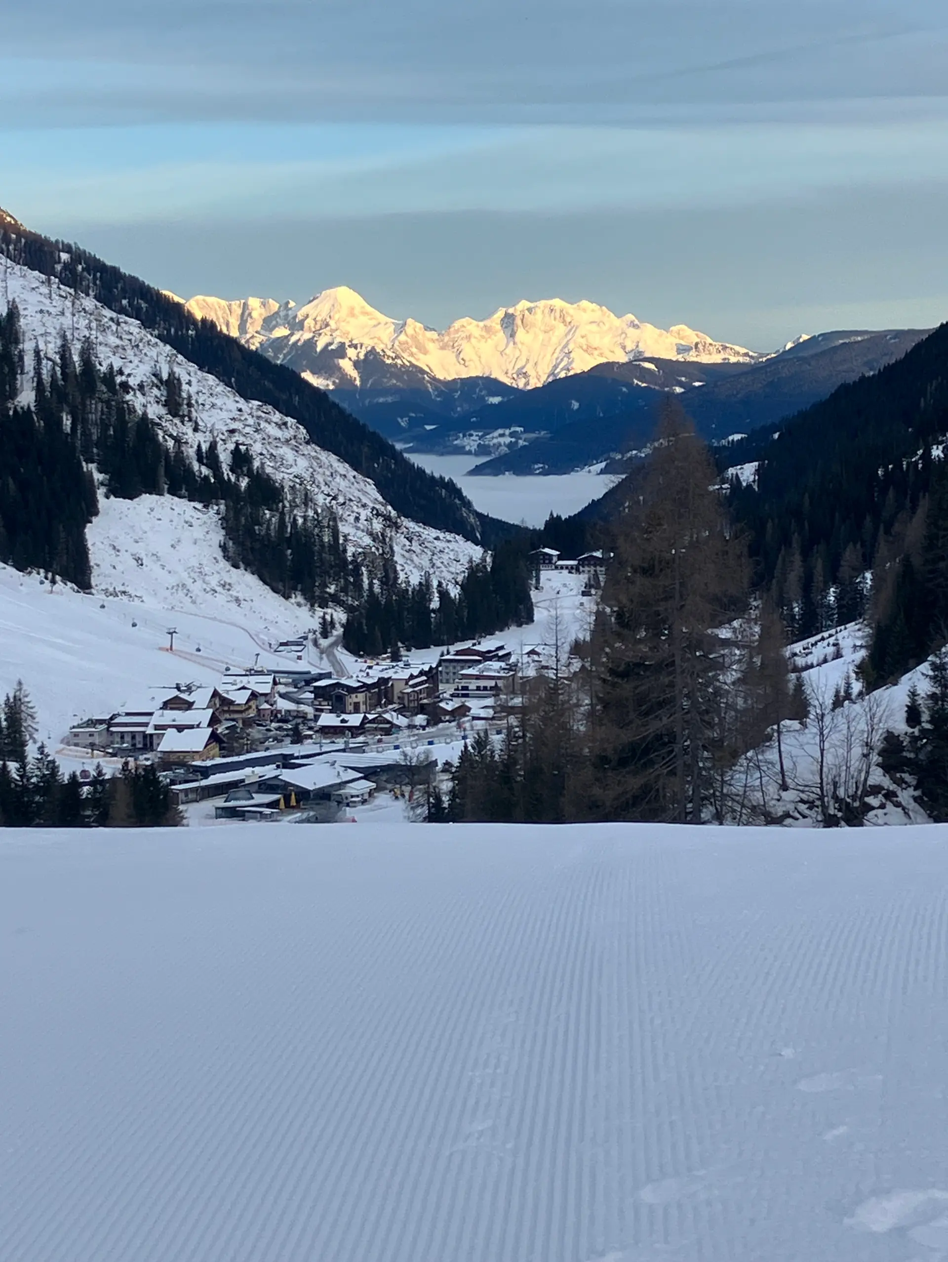 Eine winterliche Landschaft mit Bergen im Hintergrund ist zu sehen. Es liegt viel Schnee.