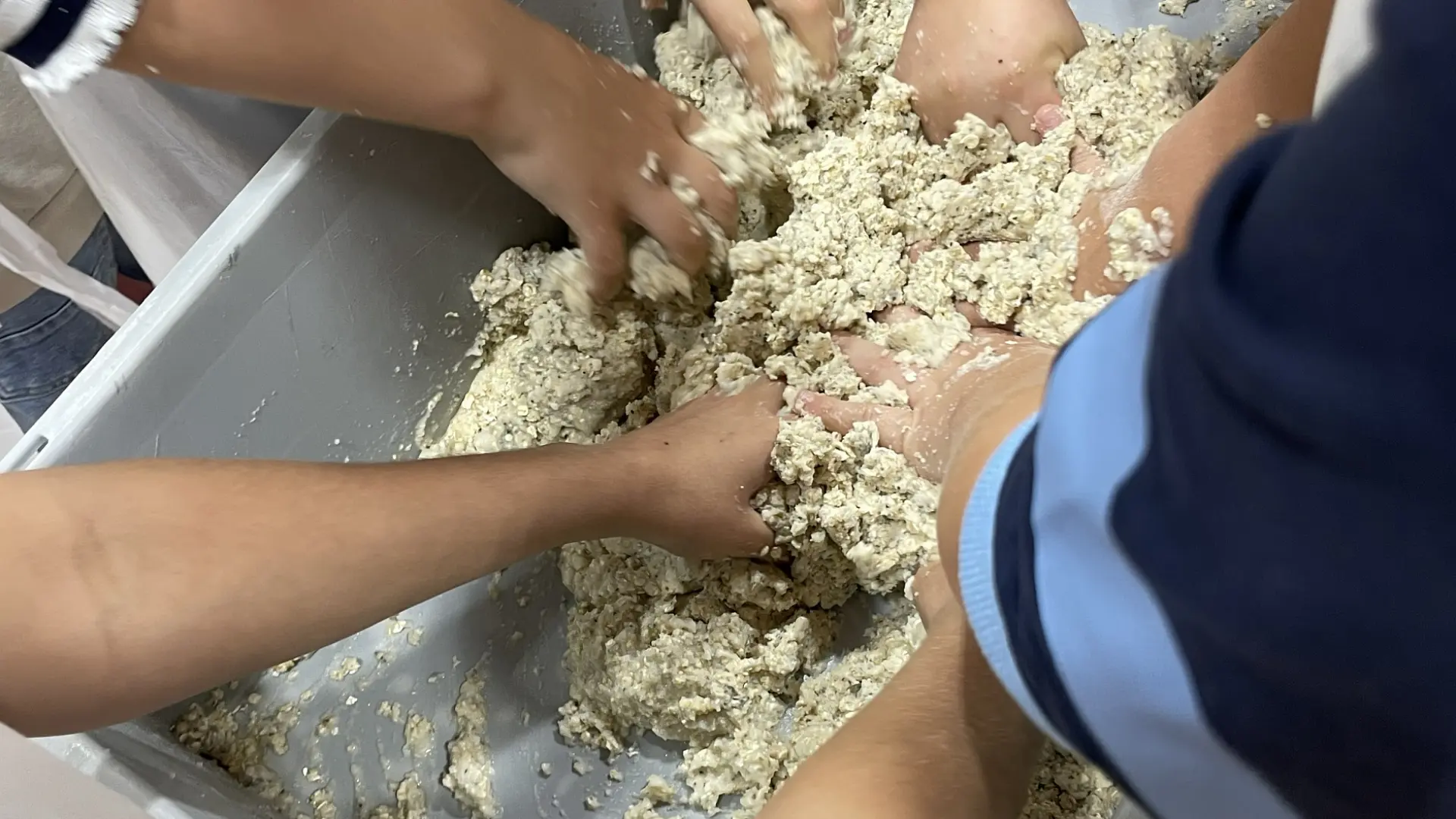 Kinderhände kneten Teig in einem großen Plastikbehälter.