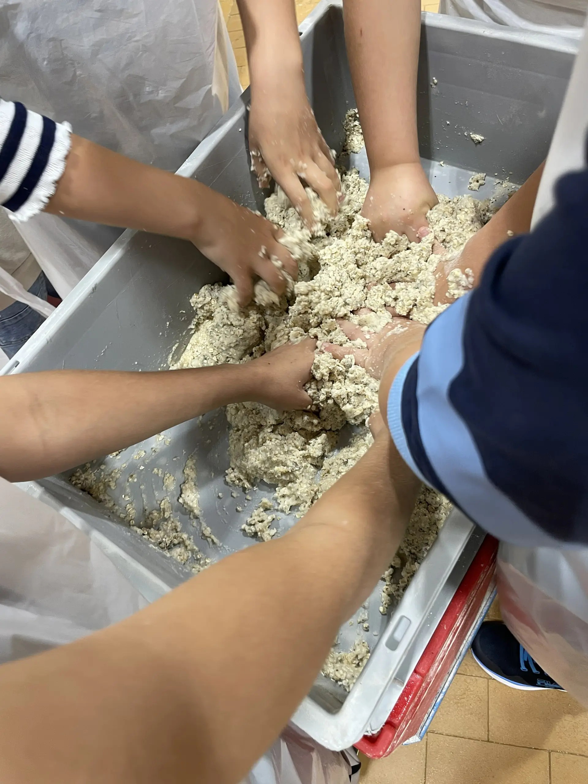 Kinderhände kneten Teig in einem großen Plastikbehälter.