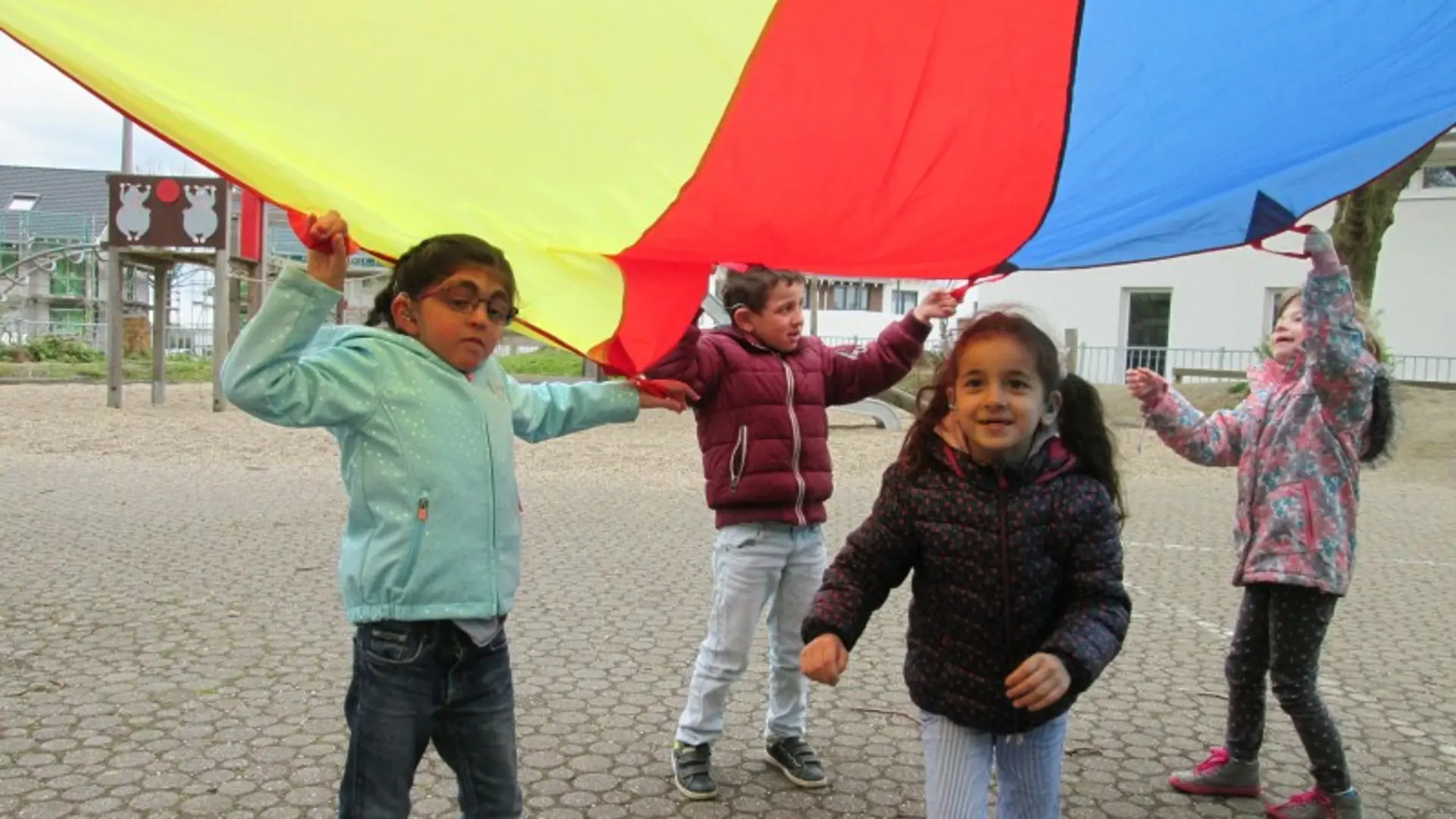 Vier Kinder spielen im Freien unter einem bunten Zelt-Tuch.