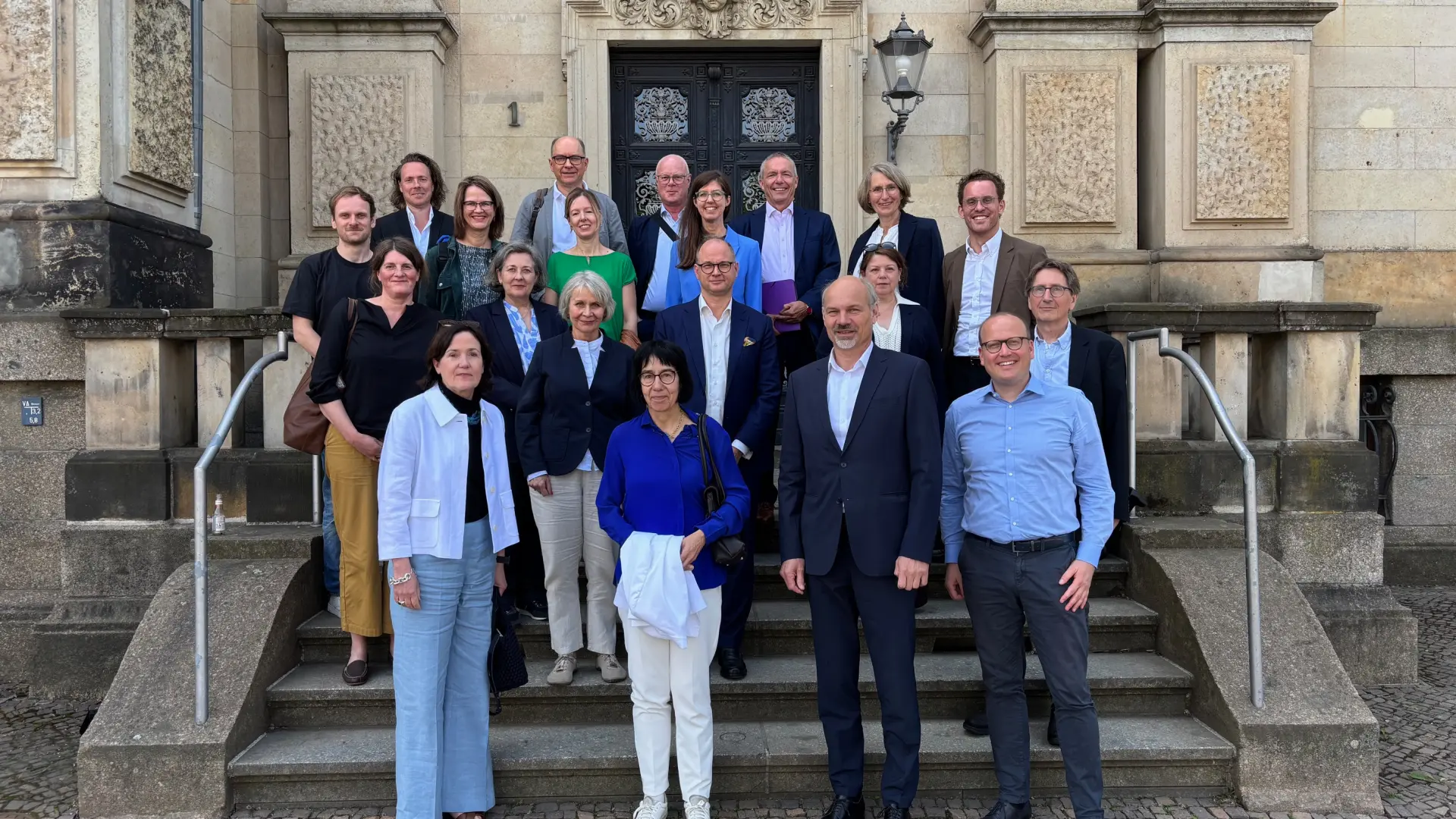 Eine Gruppe von Menschen steht auf einer Treppe, im Hintergrund die Sächsische Akademie der Wissenschaften.
