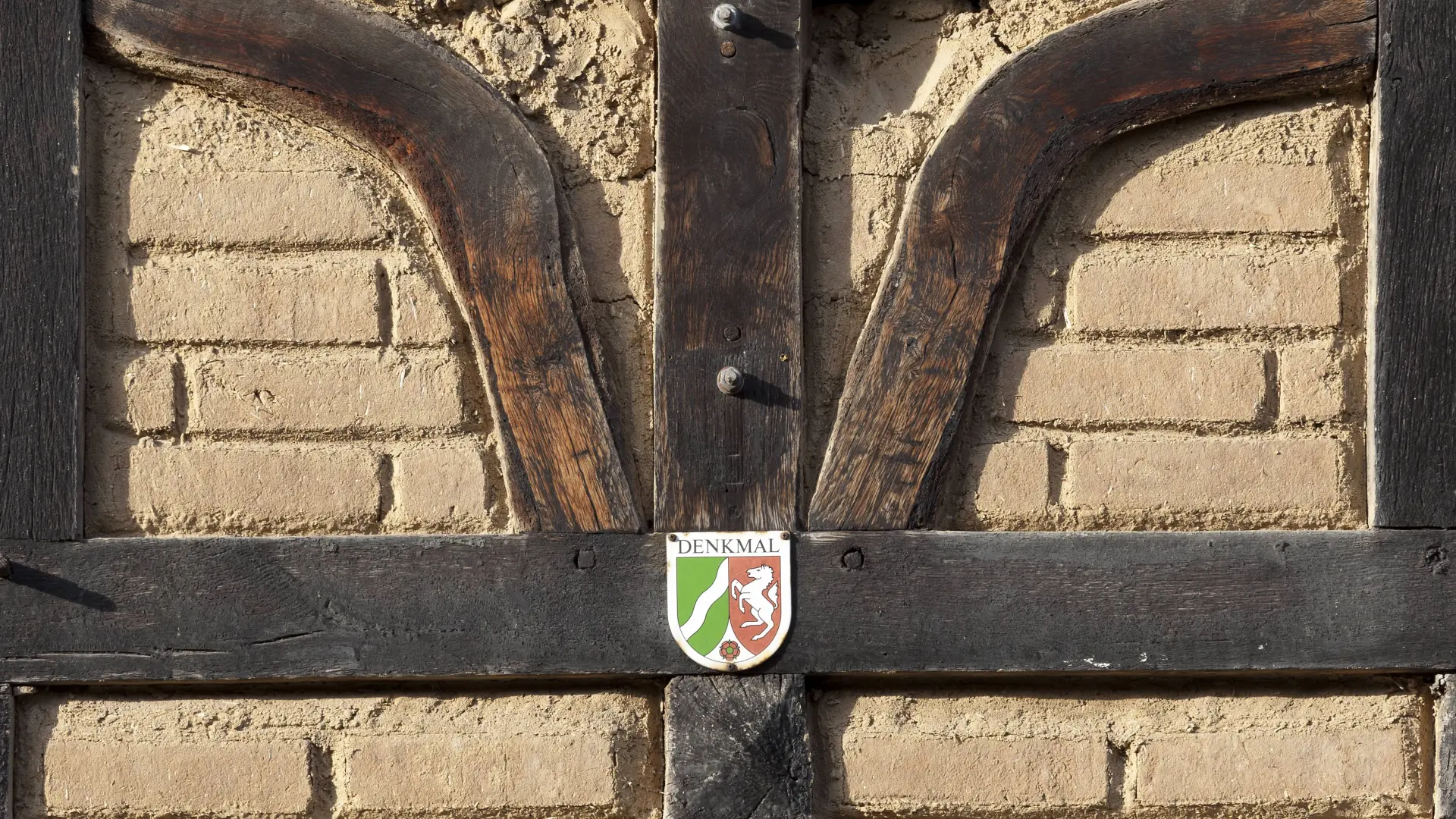 Blecherne Plakette mit NRW-Wappen, angebracht an einer Wand aus Fachwerk.