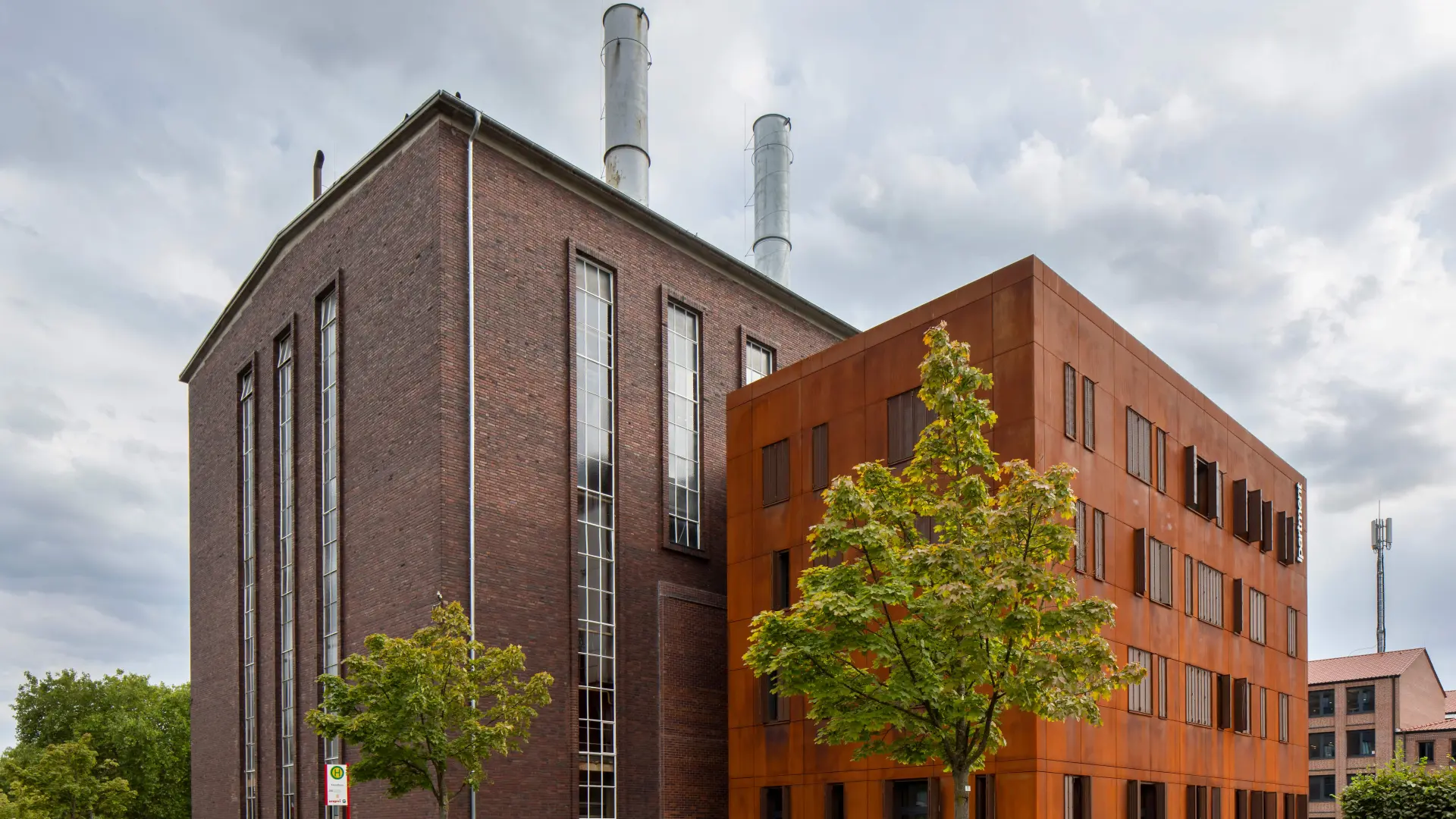 Historisches Kesselhaus des ehemaligen Eisenbahnausbesserungswerks von 1948 in Backsteinbauweise, daneben der kleinere Kubus des Neubaus von 2024 mit Cortenstahl-Fassade