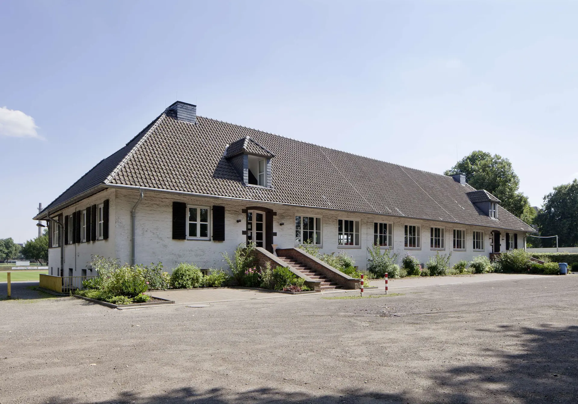 Ansicht eines eingeschossigen Gebäudes mit weiß geschlämmter Ziegelfassade und Walmdach. 