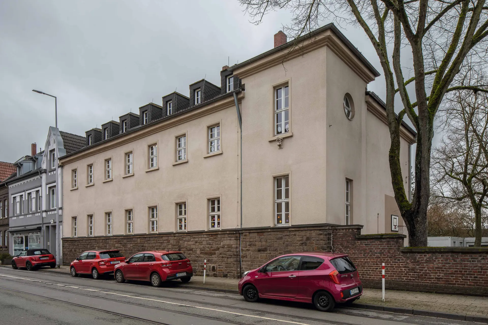 Ansicht eines innerstädtisch gelegenen, zweigeschossigen Schulgebäudes mit verputzter Fassade und Walmdach in Mülheim an der Ruhr. 