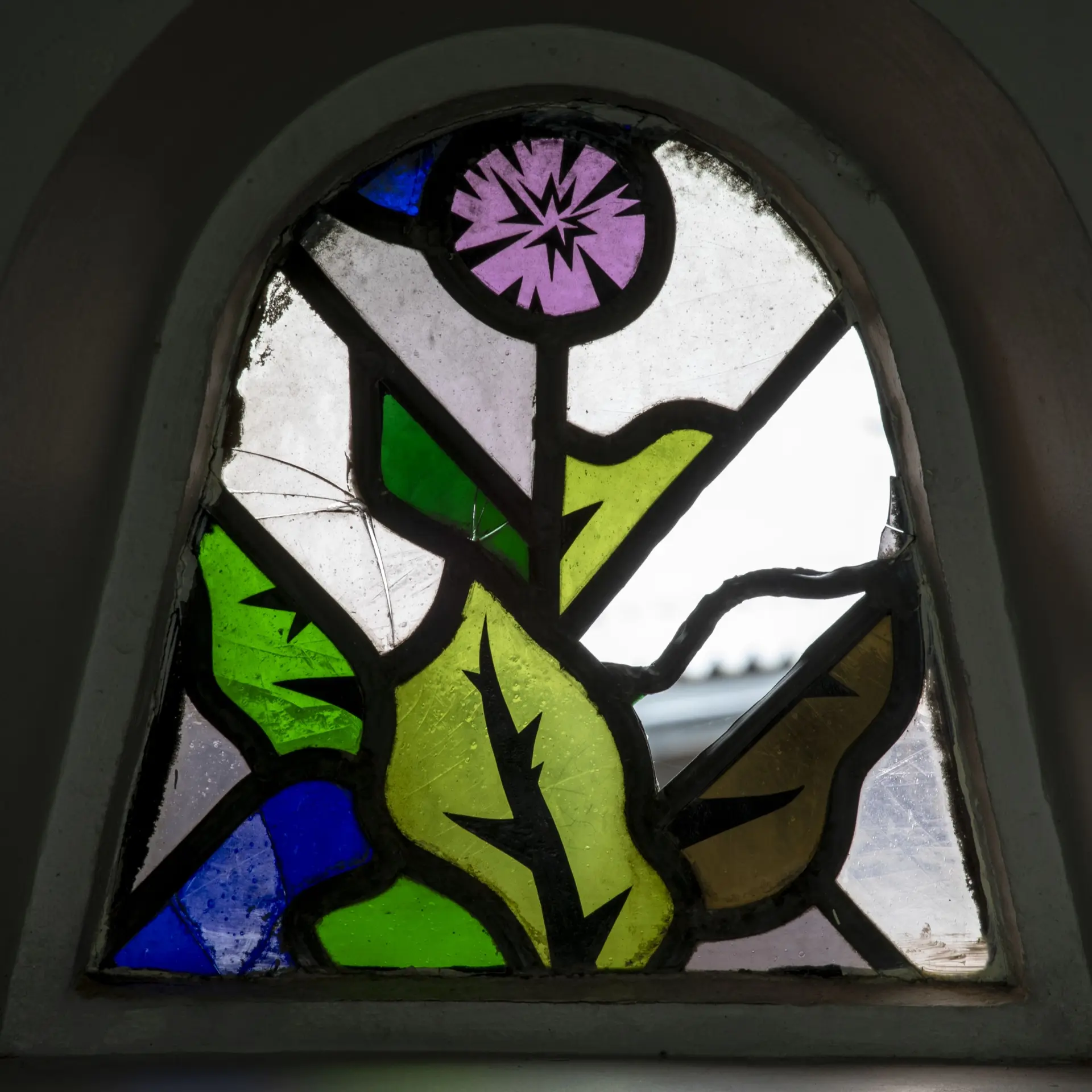 Ein glockenförmiges Fenster aus Buntglasstücken, die in Blei gefasst sind und eine Blume mit Blättern darstellen.farbiges Glasfenster aus dem Treppenhaus des Humbold-Gymnasiums in Köln mit einem Blumenmotiv.