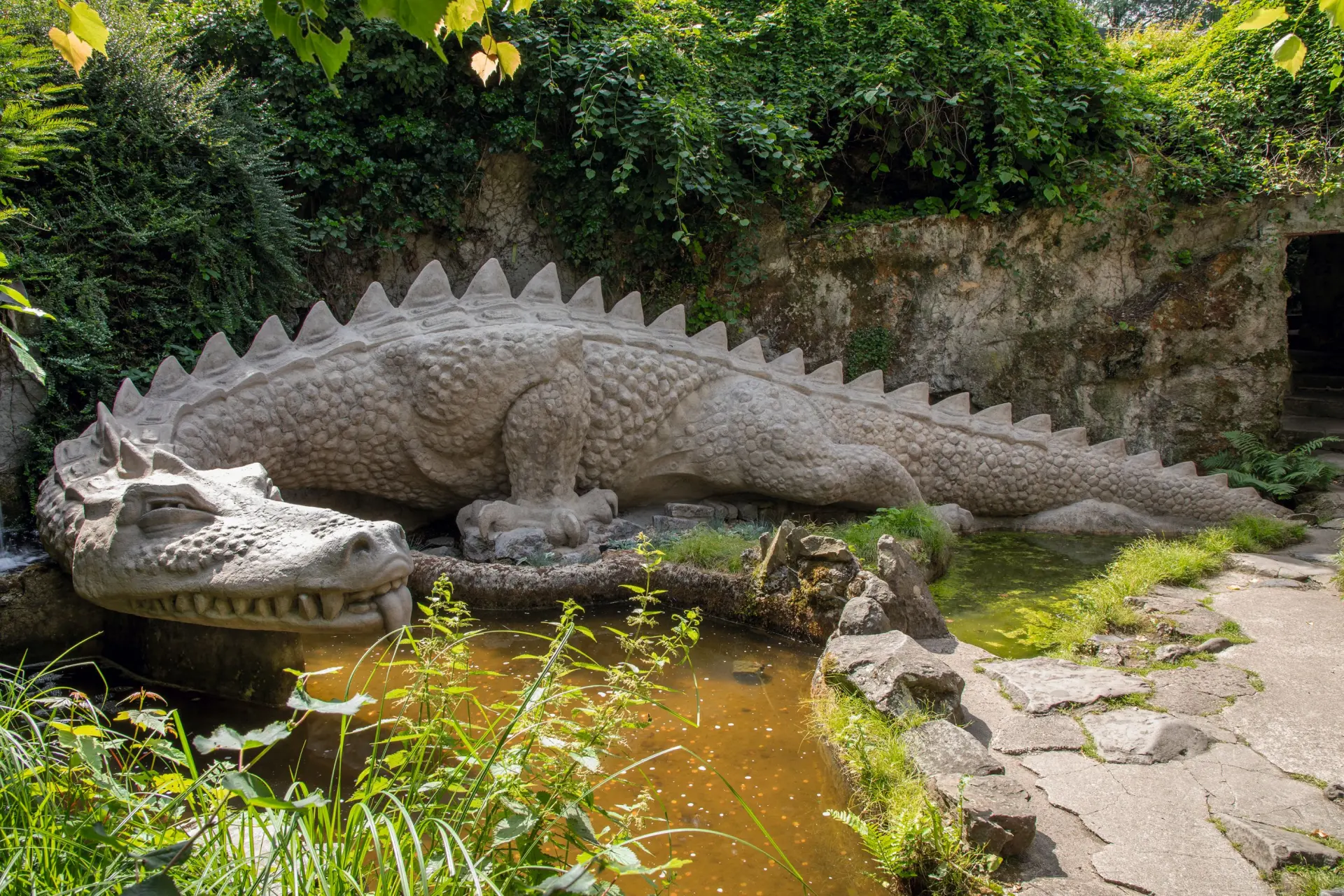 Eine sich windende Betonskulptur einer Drachenfigur mit gezacktem Rücken und schuppigem Panzer. Fafnir in der Nibelungenhalle in Königswinter.
