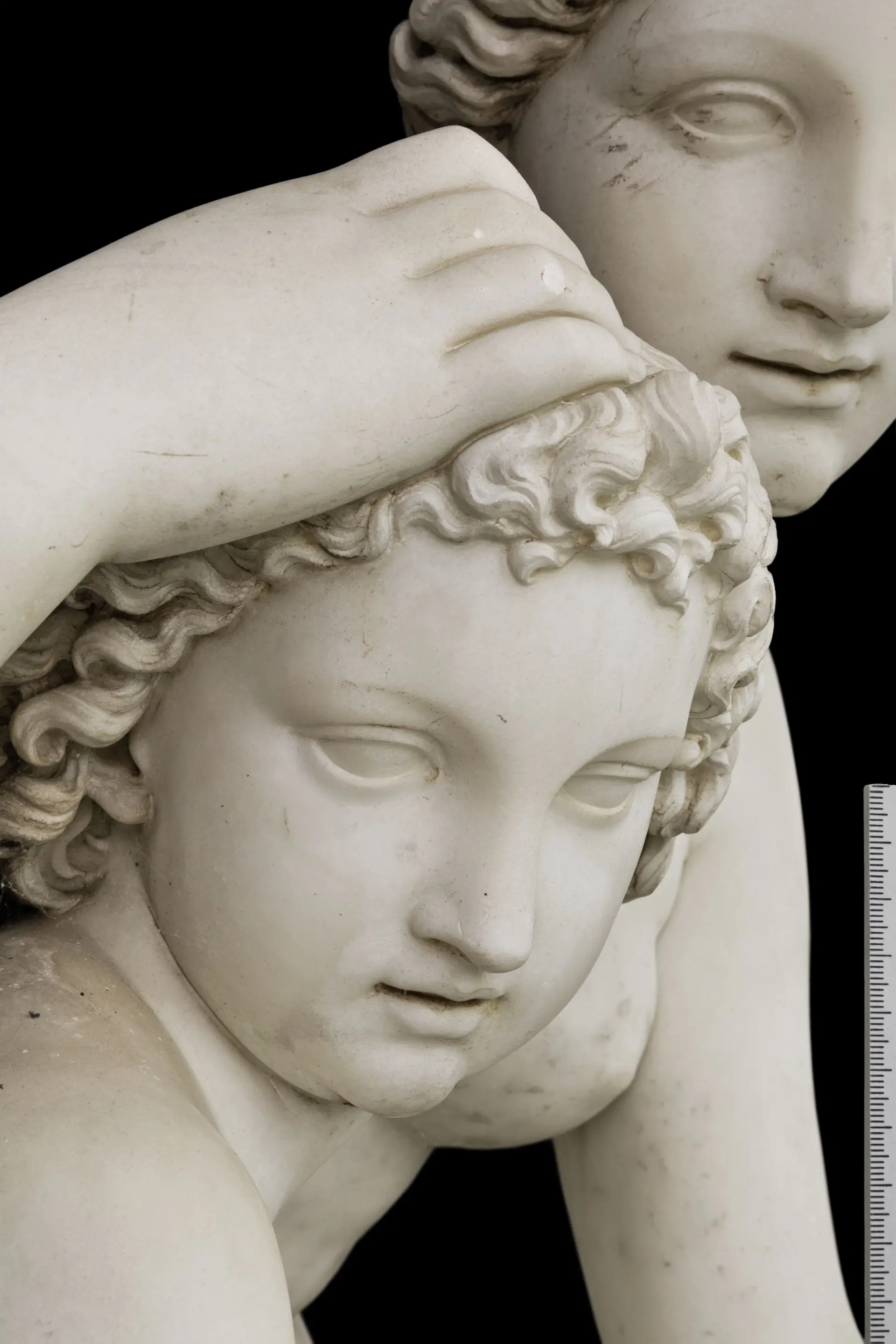 Detailansicht einer Marmorskulptur mit dem Gesicht des Armor, auf dessen Haupt die Hand der Venus ruht und dahinter das angeschnittene Gesicht der Venus.