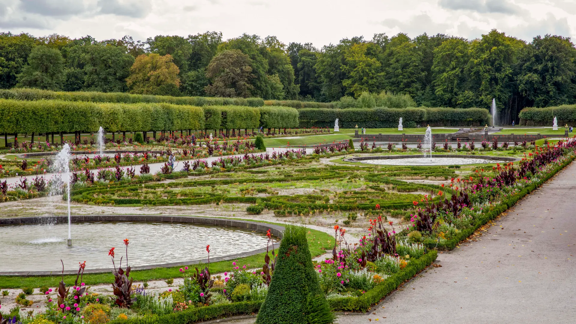 von Hitze und Dürre geschädigte Blumenbeete, dazwischen Gartenfontänen 