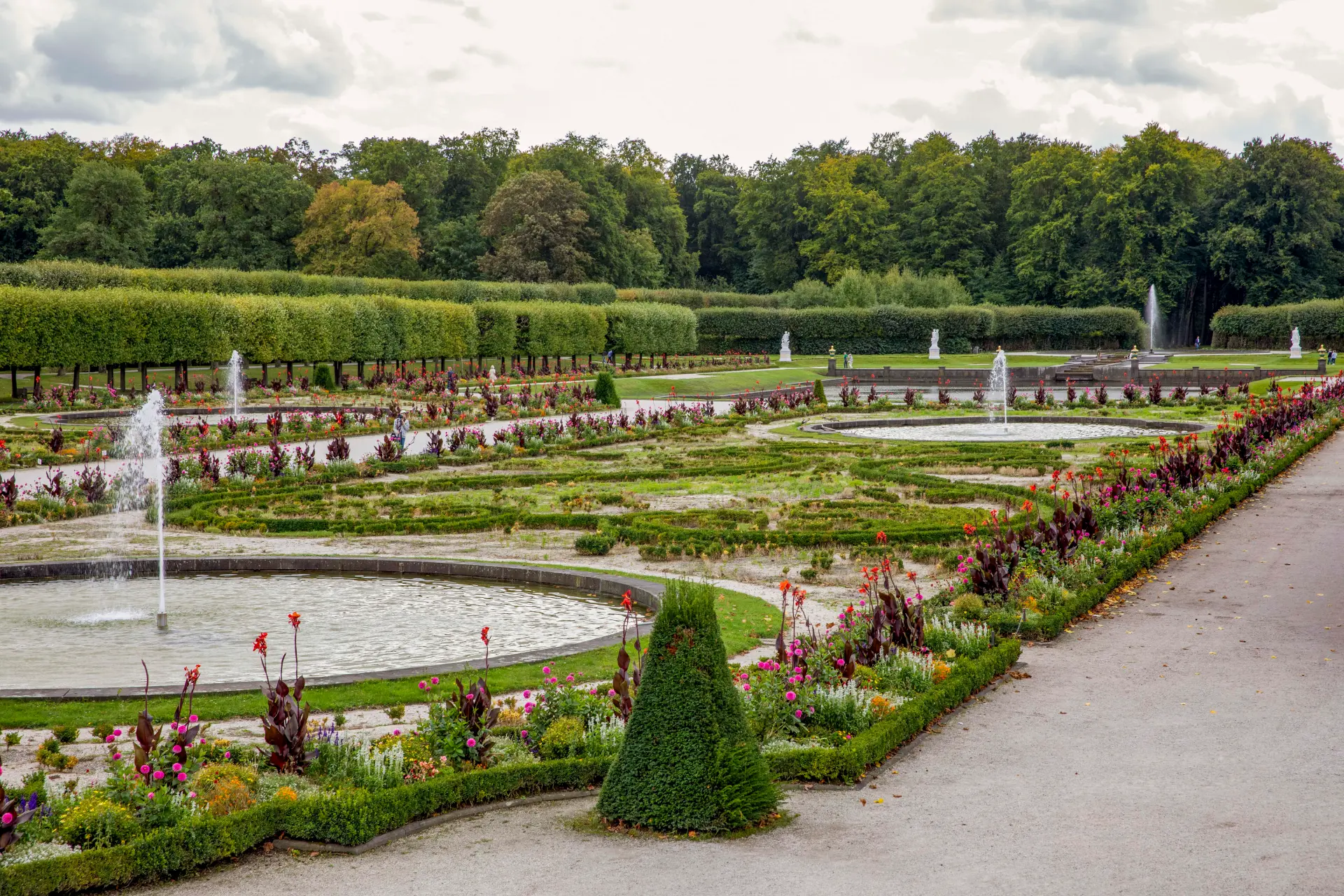 von Hitze und Dürre geschädigte Blumenbeete, dazwischen Gartenfontänen 