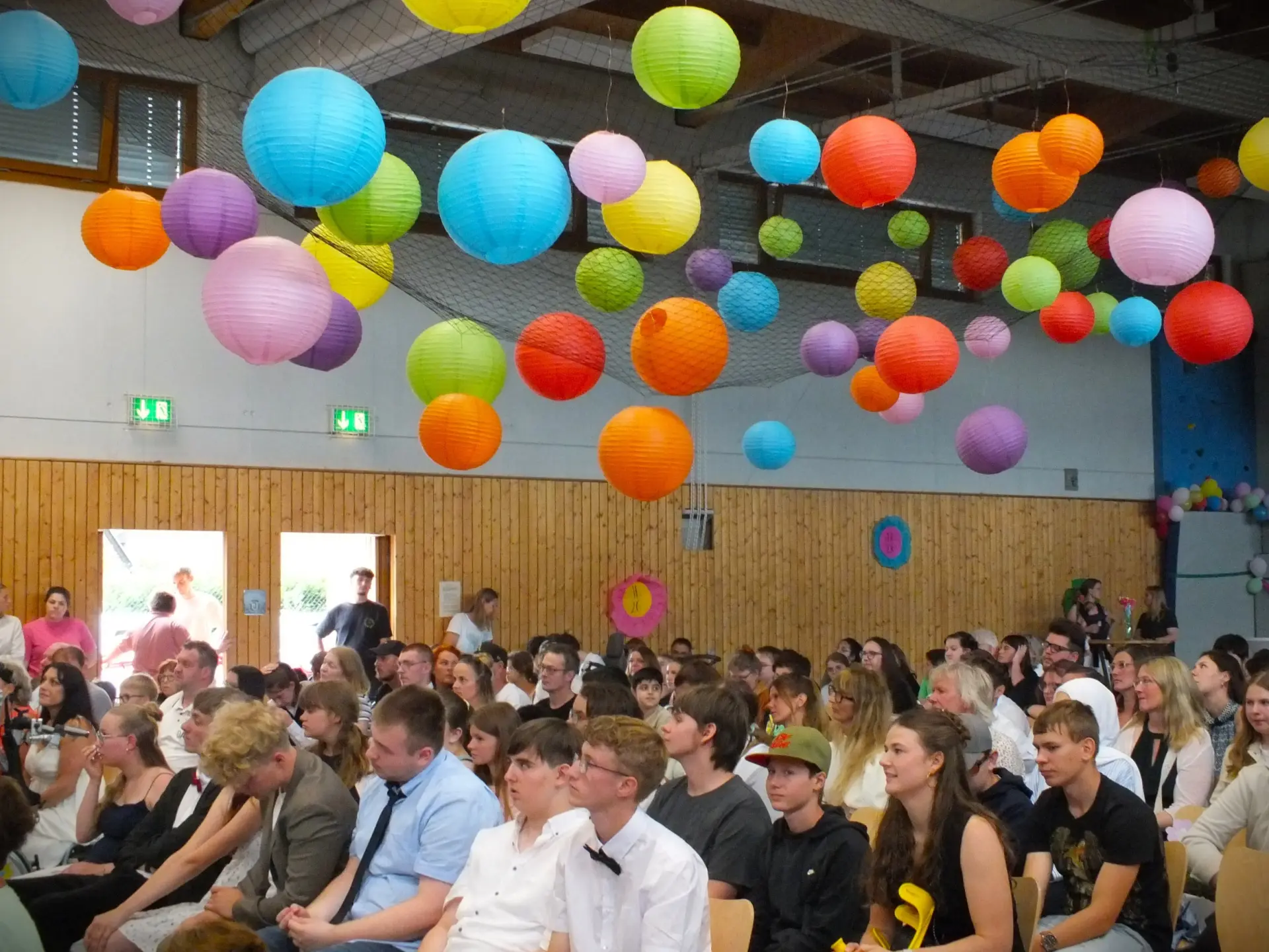 In einer mit bunten Lampions geschmückten Turnhalle sitzen viele Menschen im bestuhlten Innenraum