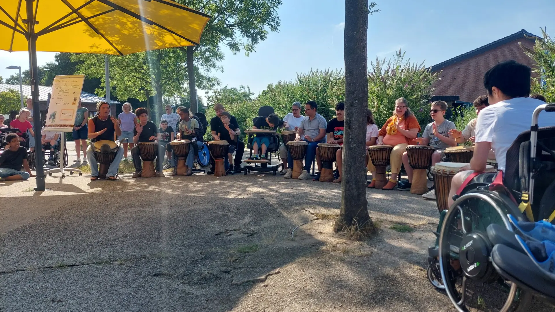 Eine Gruppe Jugendlicher, zum Teil im Rollstuhl, sitzt im Kreis im Freien und trommelt