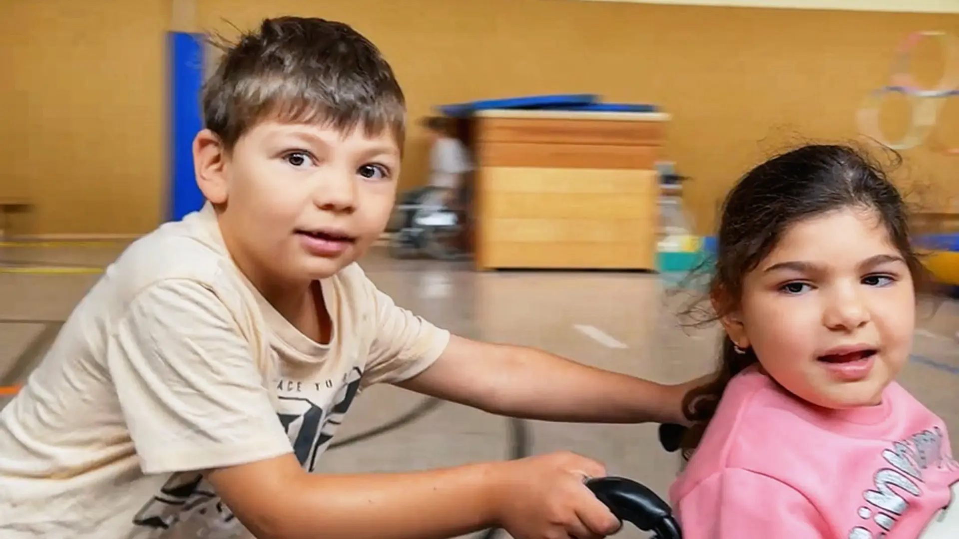 Bild von 2 Kindern. Eines der Kinder sitzt in einem Rollstuhl.