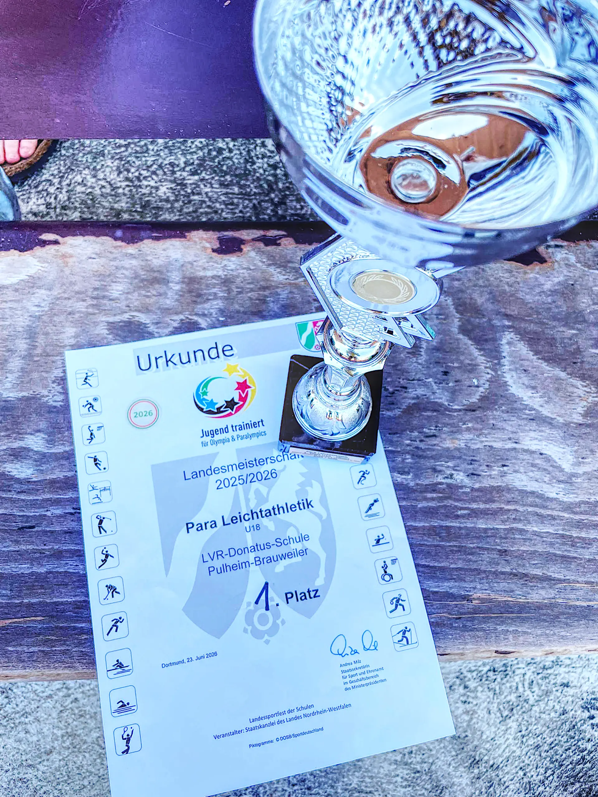 Bild von einem Pokal und einer Urkunde. Auf der Urkunde steht Platz 1.