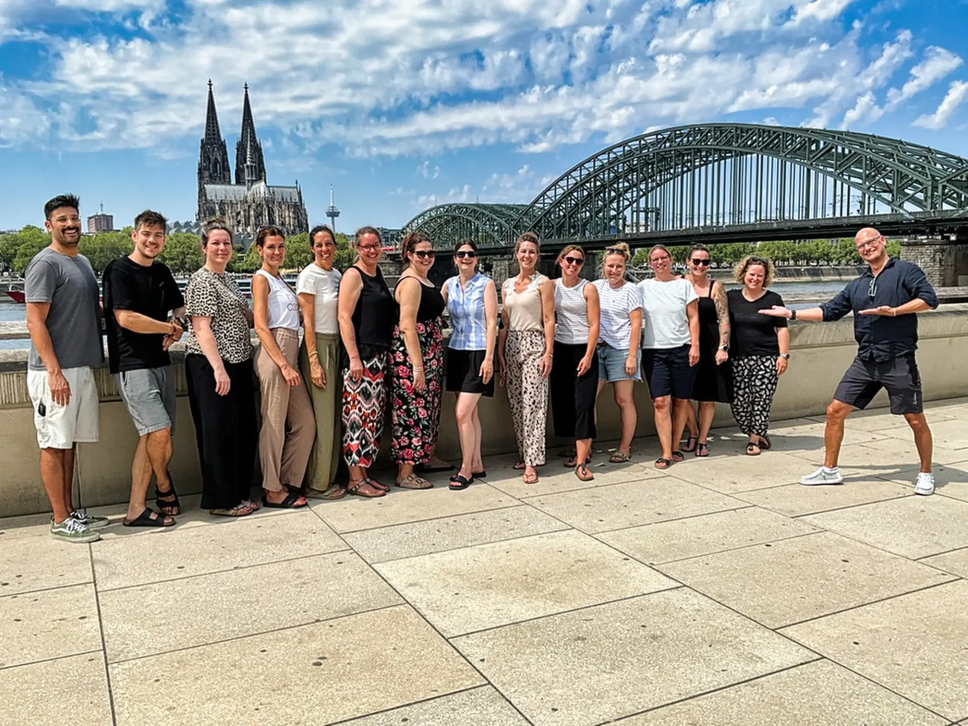 Bild von 15 Personen, die nebeneinander am Rheiunfer stehen. Im Hintergrund ist der Rhein zu sehen.