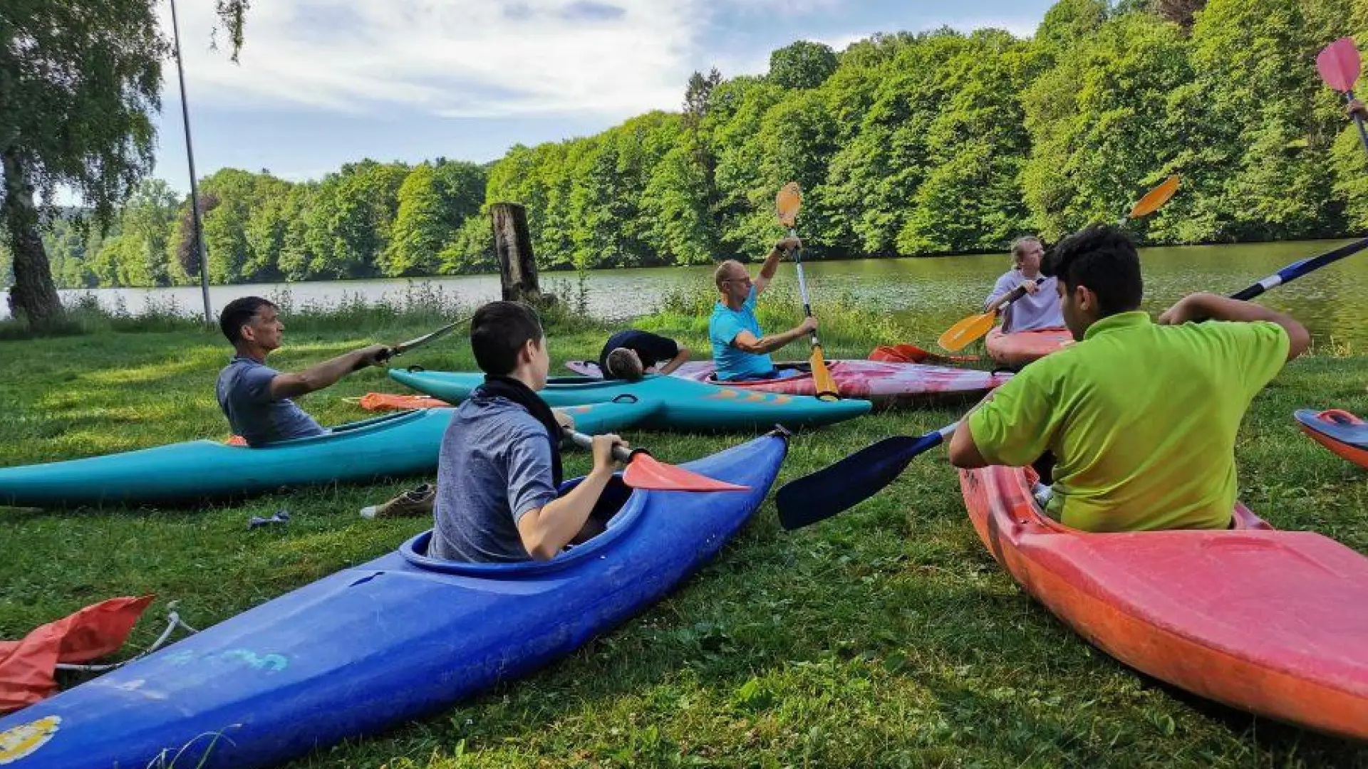 Sport-Challenge: Schüler*innen sitzen in bunten Kanus auf dem Rasen und üben das Paddeln