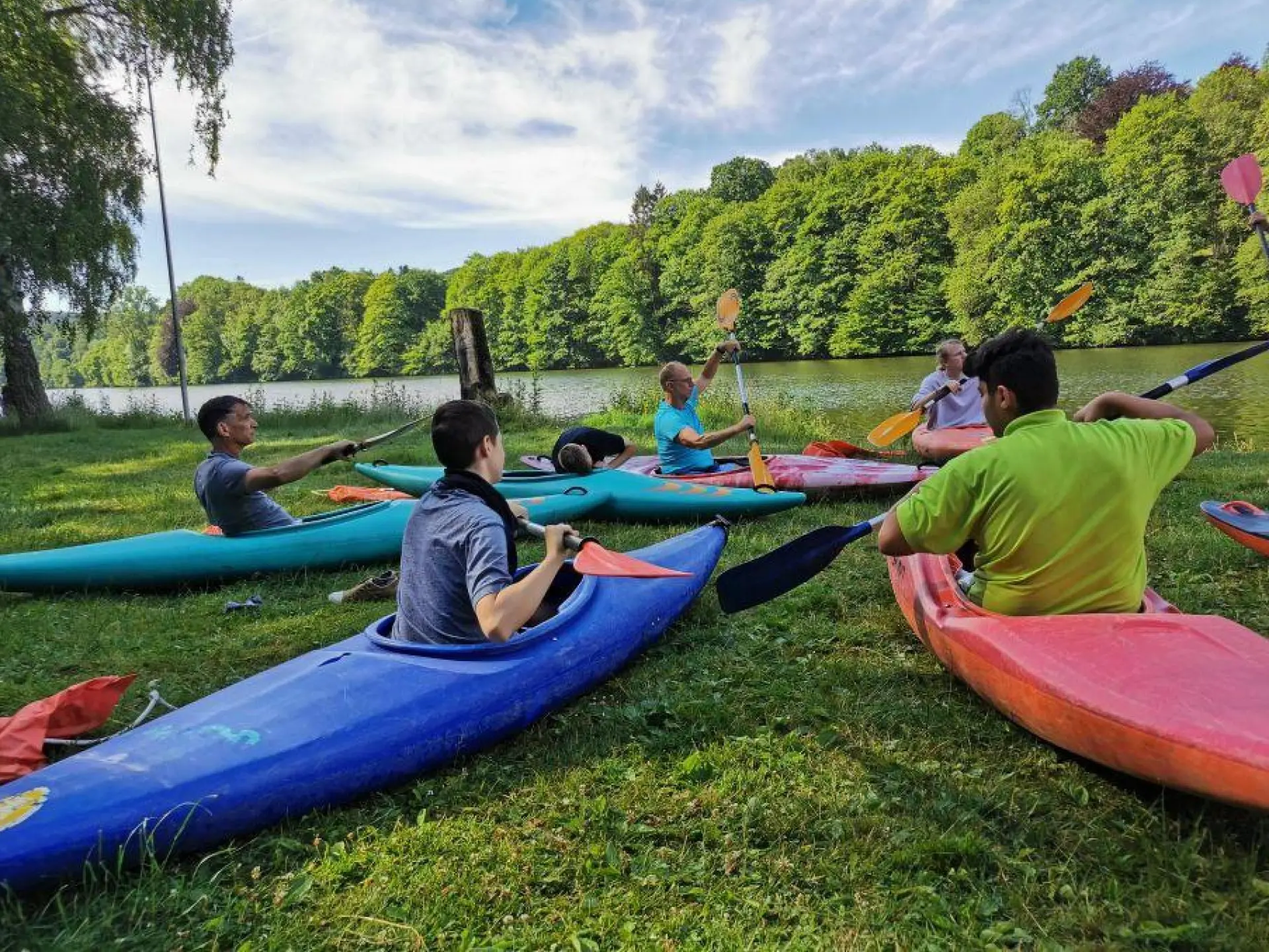 Sport-Challenge: Schüler*innen sitzen in bunten Kanus auf dem Rasen und üben das Paddeln