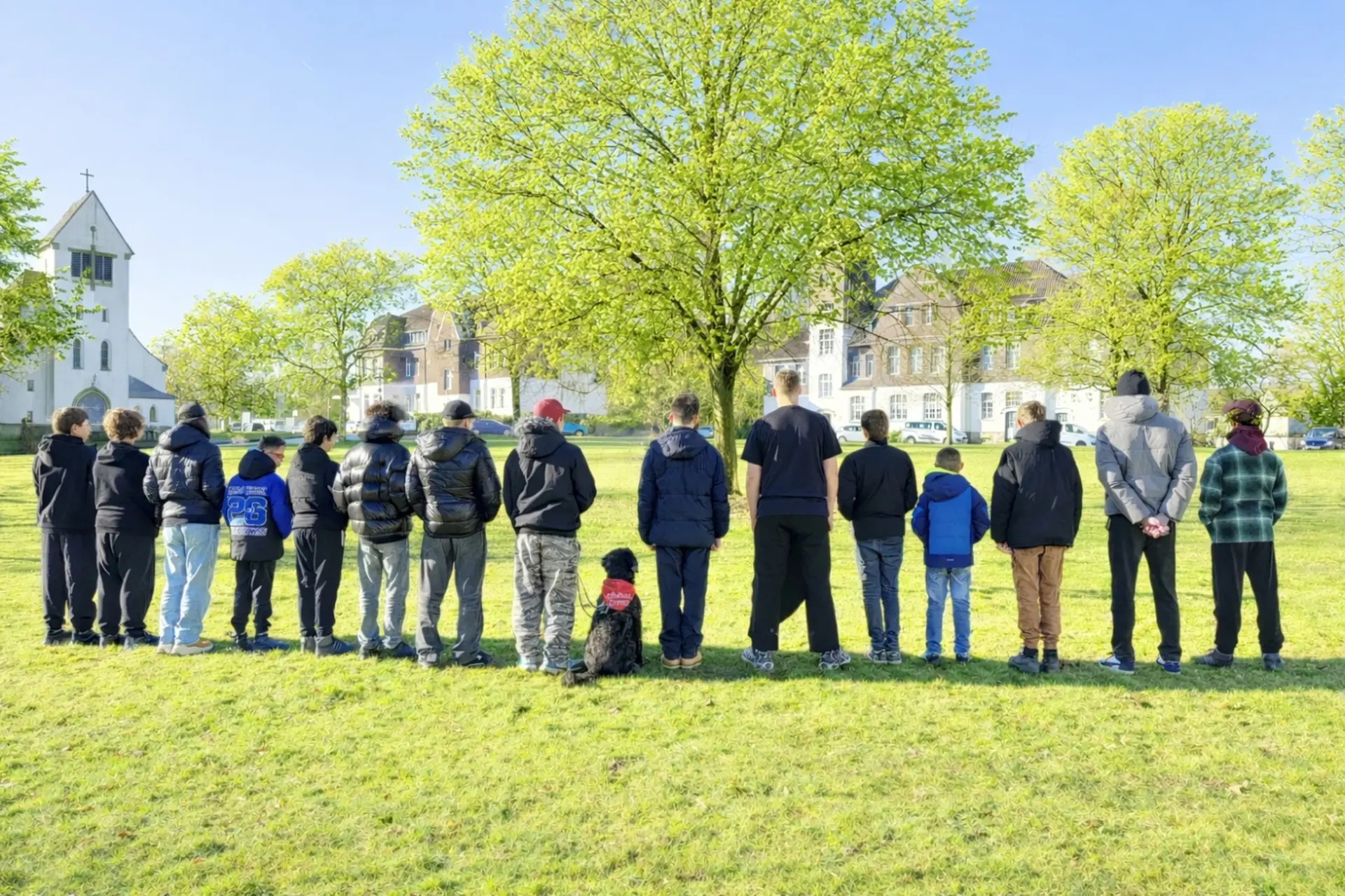 Mehrere Schüler*innen stehen mit dem Rücken zur Kamera auf einer Wiese auf dem Schulgelände