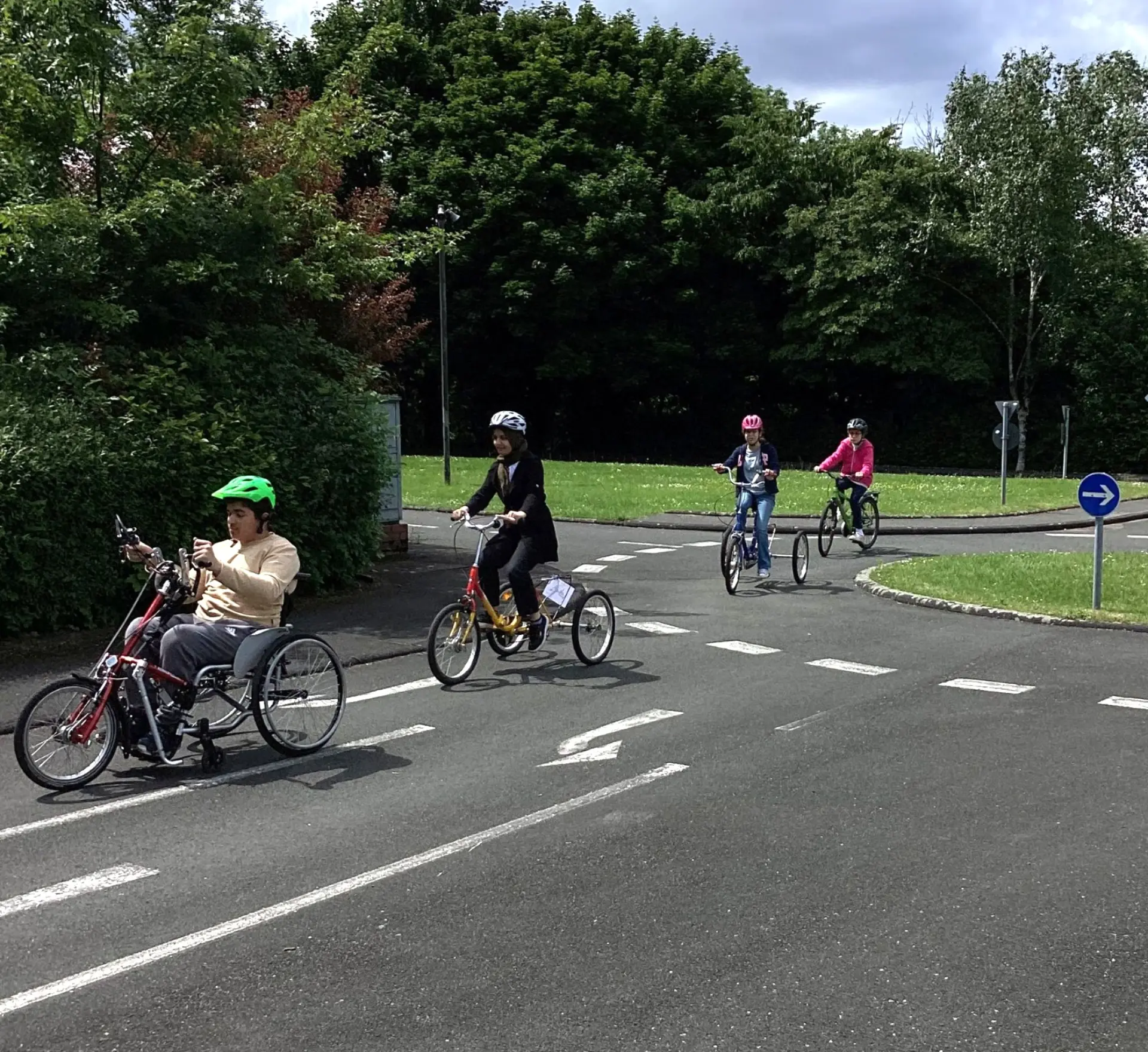 Auf einem Verkehrsübungsplatz fahren Jugendliche mit einem Handbike, zwei großen Dreirädern und einem Fahrrad