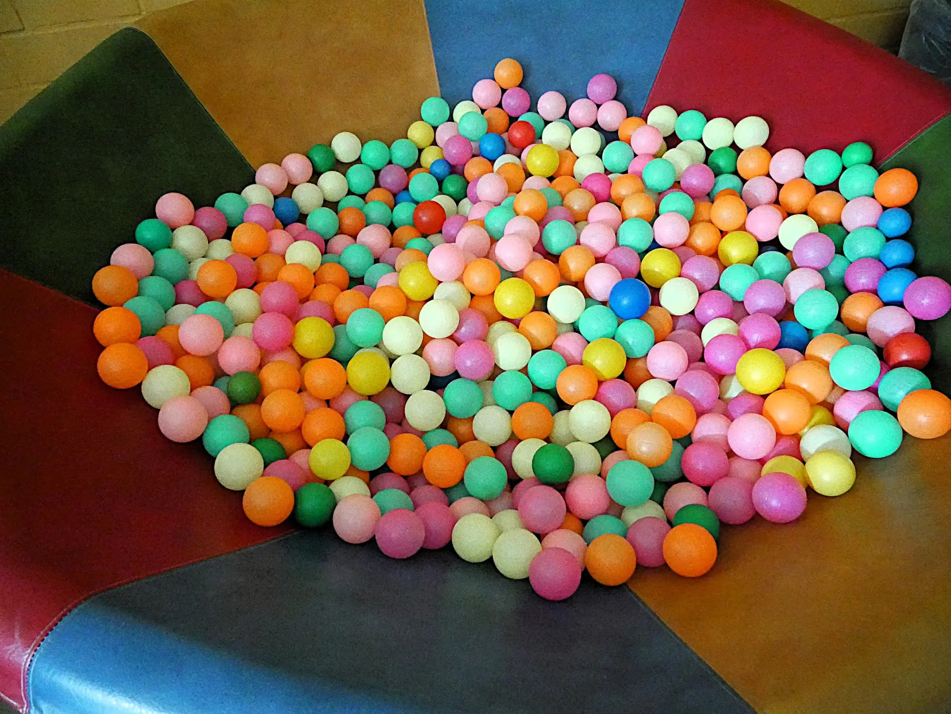 Blick von oben auf eine große, bunte Sitzmulde, die komplett mit vielen kleinen Kunststoffbällen in Pastelltönen gefüllt ist.