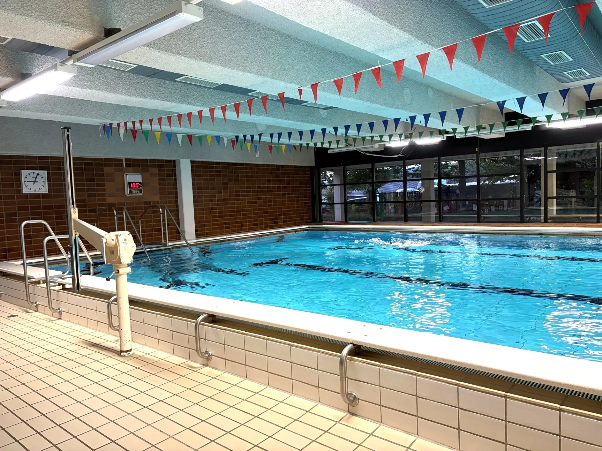 Blick in ein Schwimmbad mit bunten Wimpeln an der Decke: im Vordergrund ein Schwimmbad-Lifter