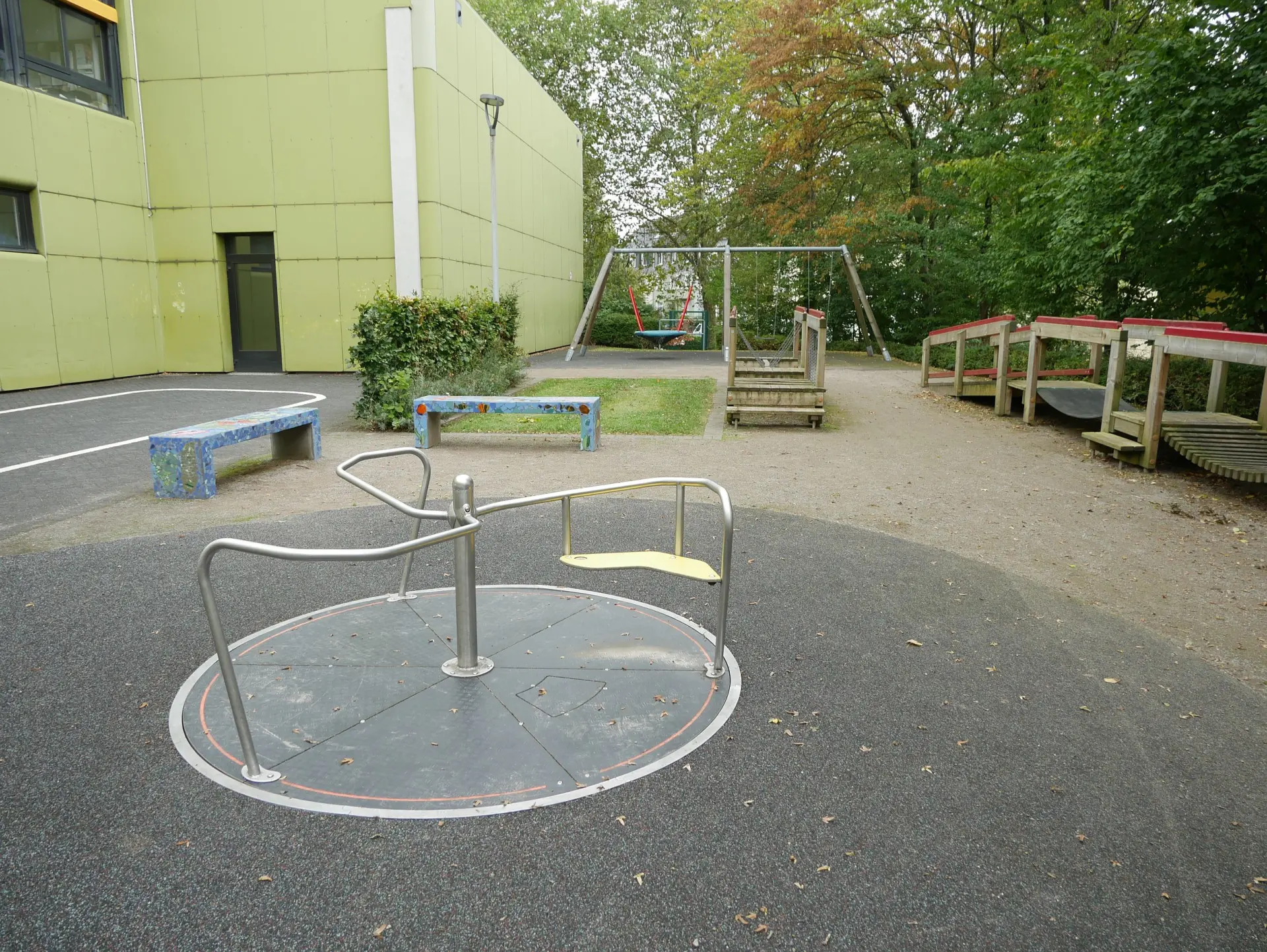 Ein barrierefreies, bodenebenes Metallkarussell auf einer dunklen Schutzfläche im Außenbereich der Schule.