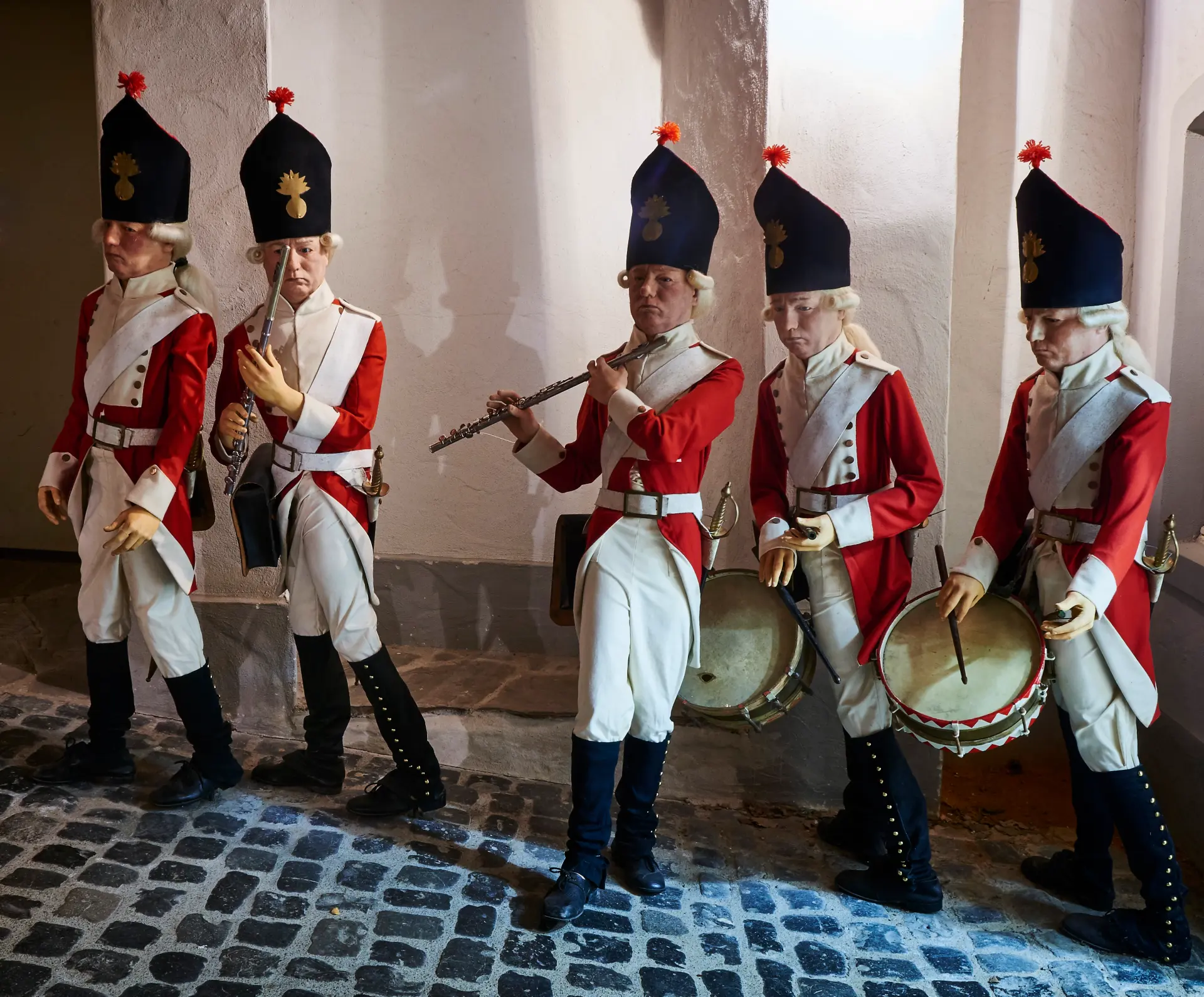 Foto: Szene aus der Ausstellung mit fünf Figuren einer historischen Militärkapelle in roten Uniformen mit Trommeln und Flöten.