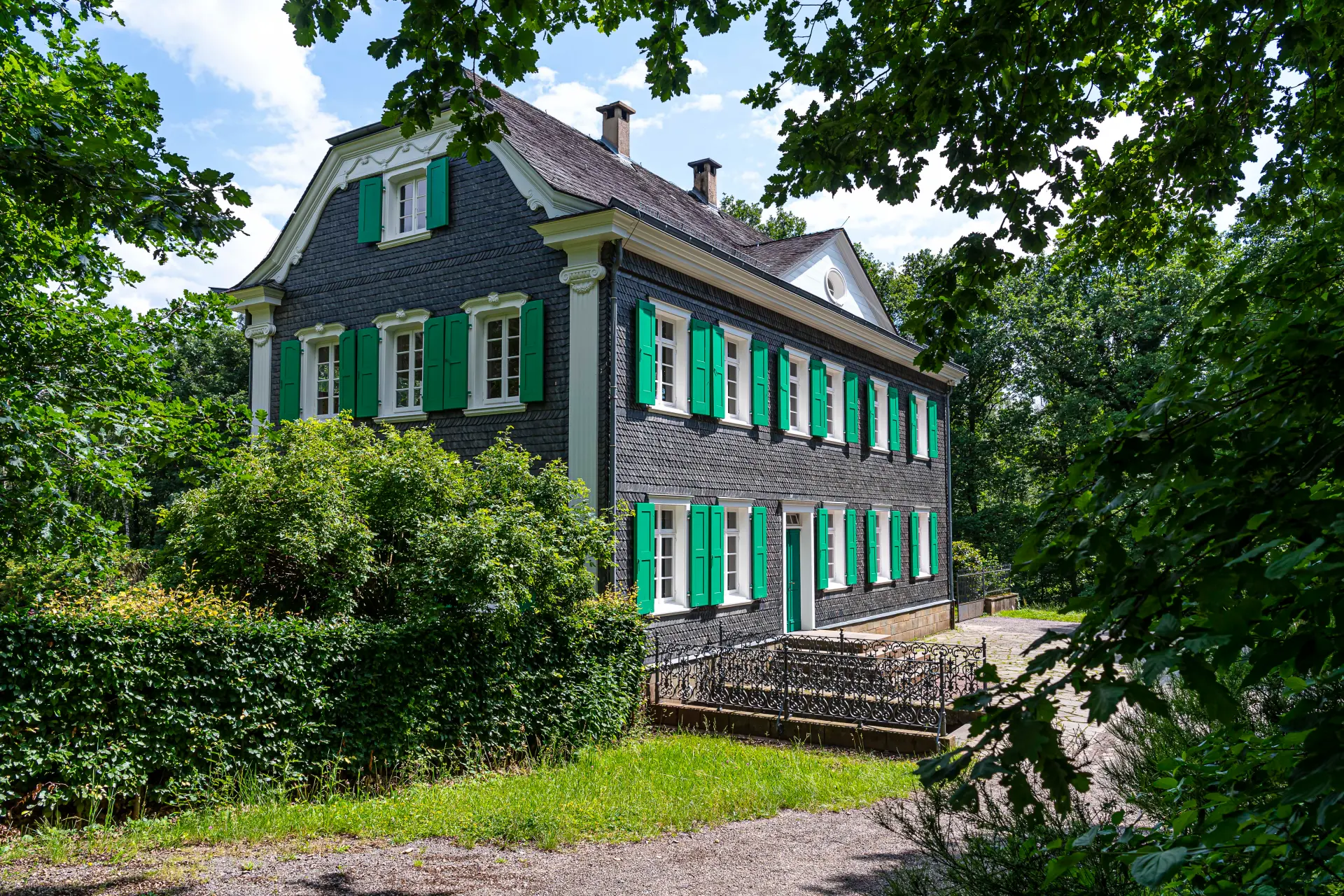 Zweistöckiges Haus mit Schindelfassade, weißen Fenstern und grünen Fensterläden.