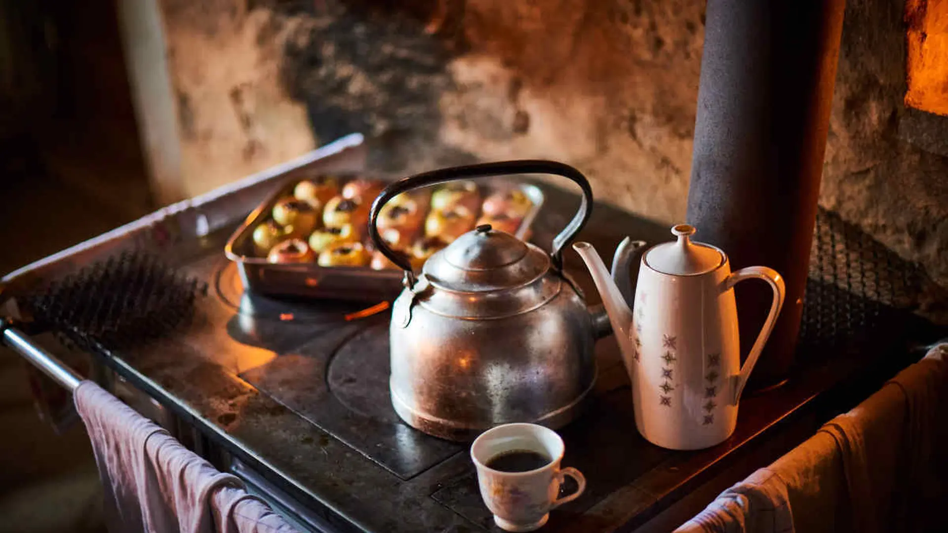 Ein Teekessel, eine Tasse und Äpfel auf einem Herd.