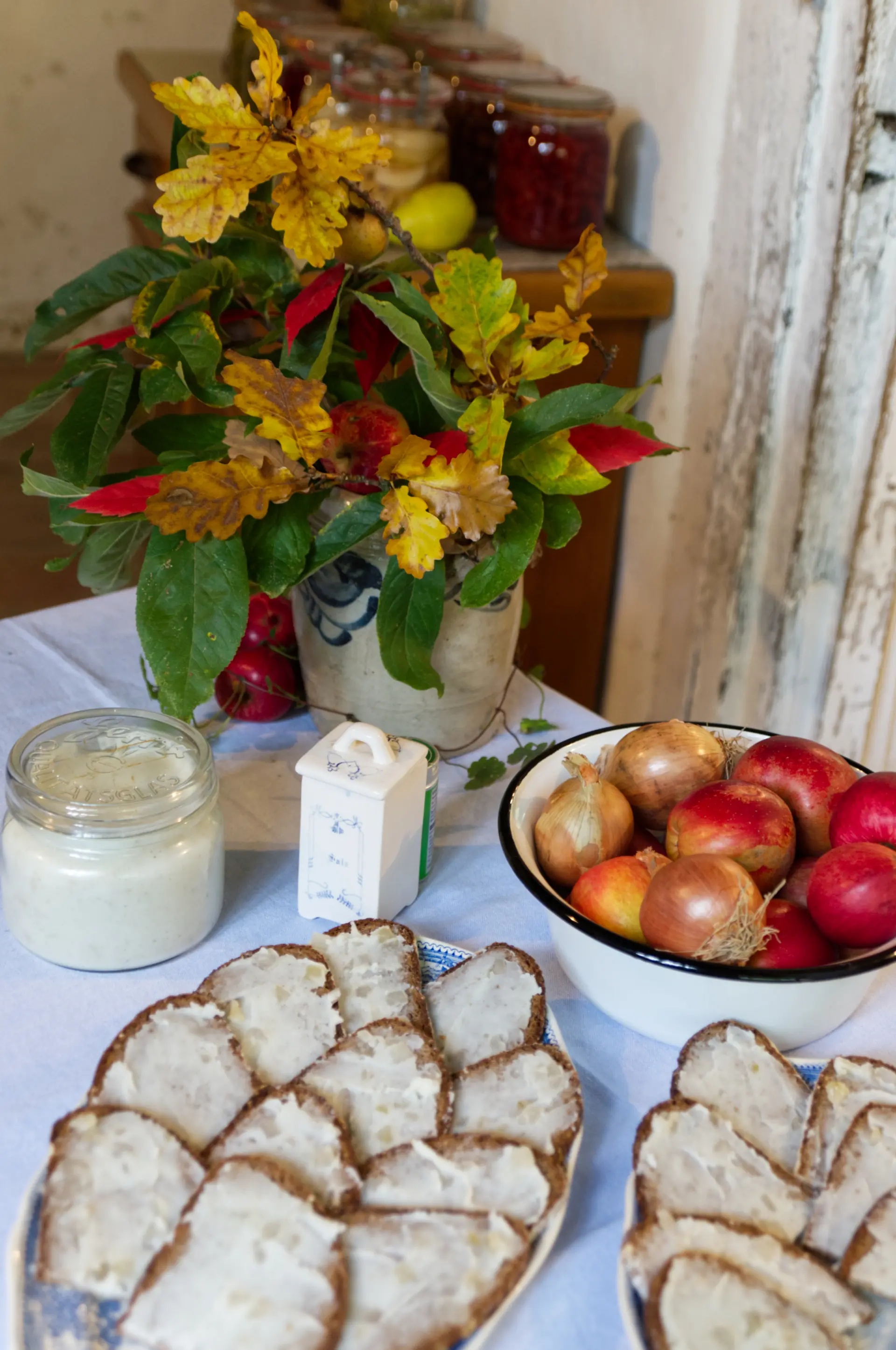 Geschmierte Brote, Äpfel, Zwiebeln und Blumen auf einem Tisch.