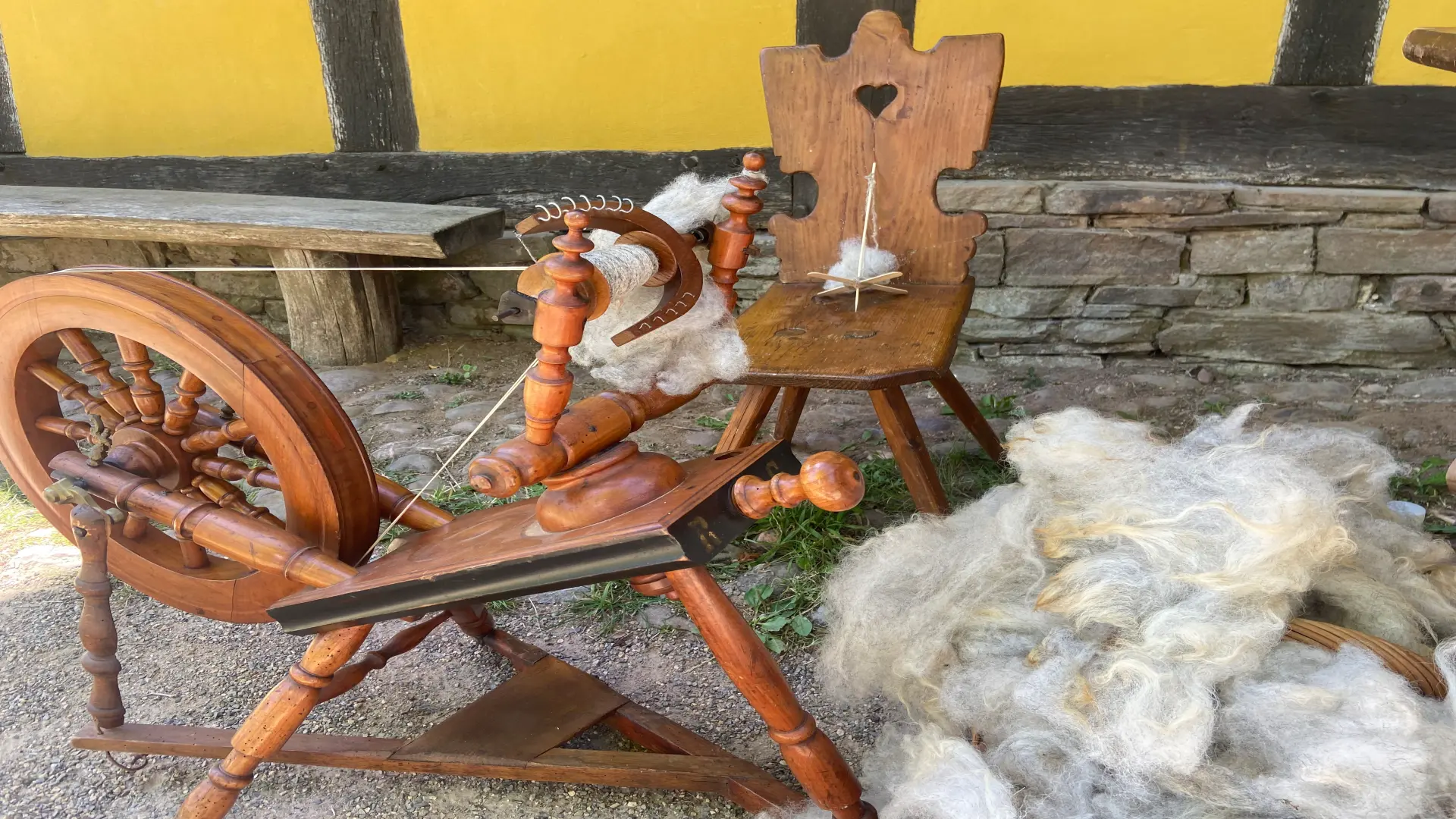 Eine Handspindel mit einem Korb Wolle daneben.