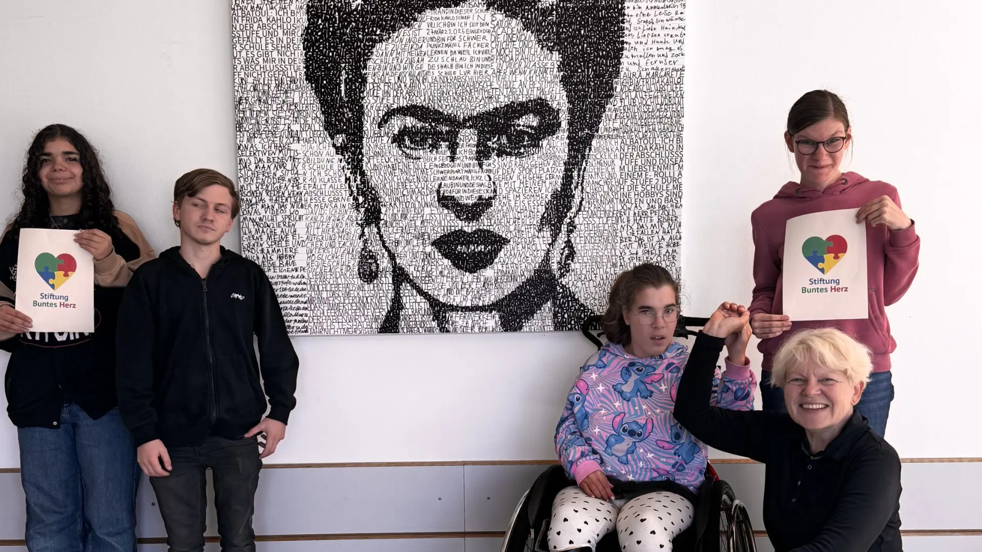 Mehrere Personen im Schulfoyer vor einem großen Porträt von Frida Kahlo.