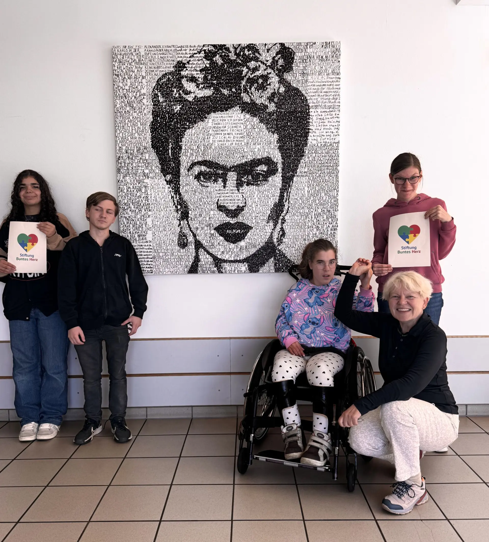 Vier Schüler*innen und eine erwachsene Person stehen vor dem aufgehangenen Porträtbild von Frida Kahlo.