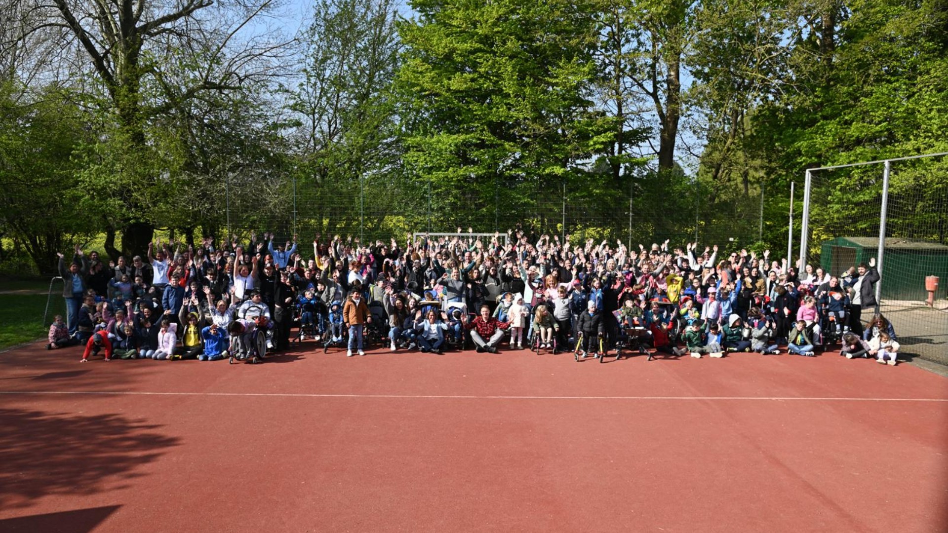 Gruppenfoto der Schulgemeinschaft auf einem Ascheplatz, im Hintergrund sind viele Bäume.