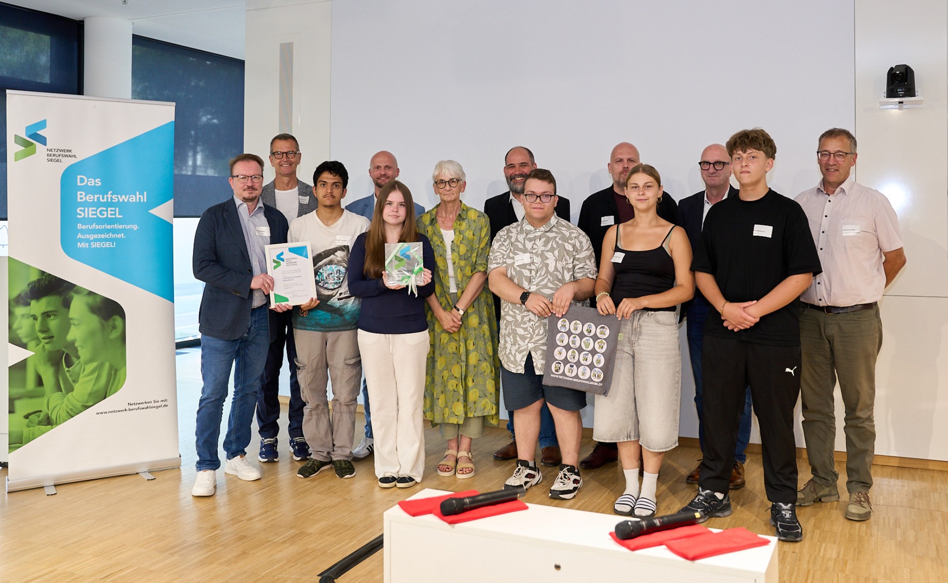 Eine Gruppe von Schüler*innen und Lehrkräften präsentiert stolz das verliehene Berufswahl-Siegel für ausgezeichnete Berufsorientierung.