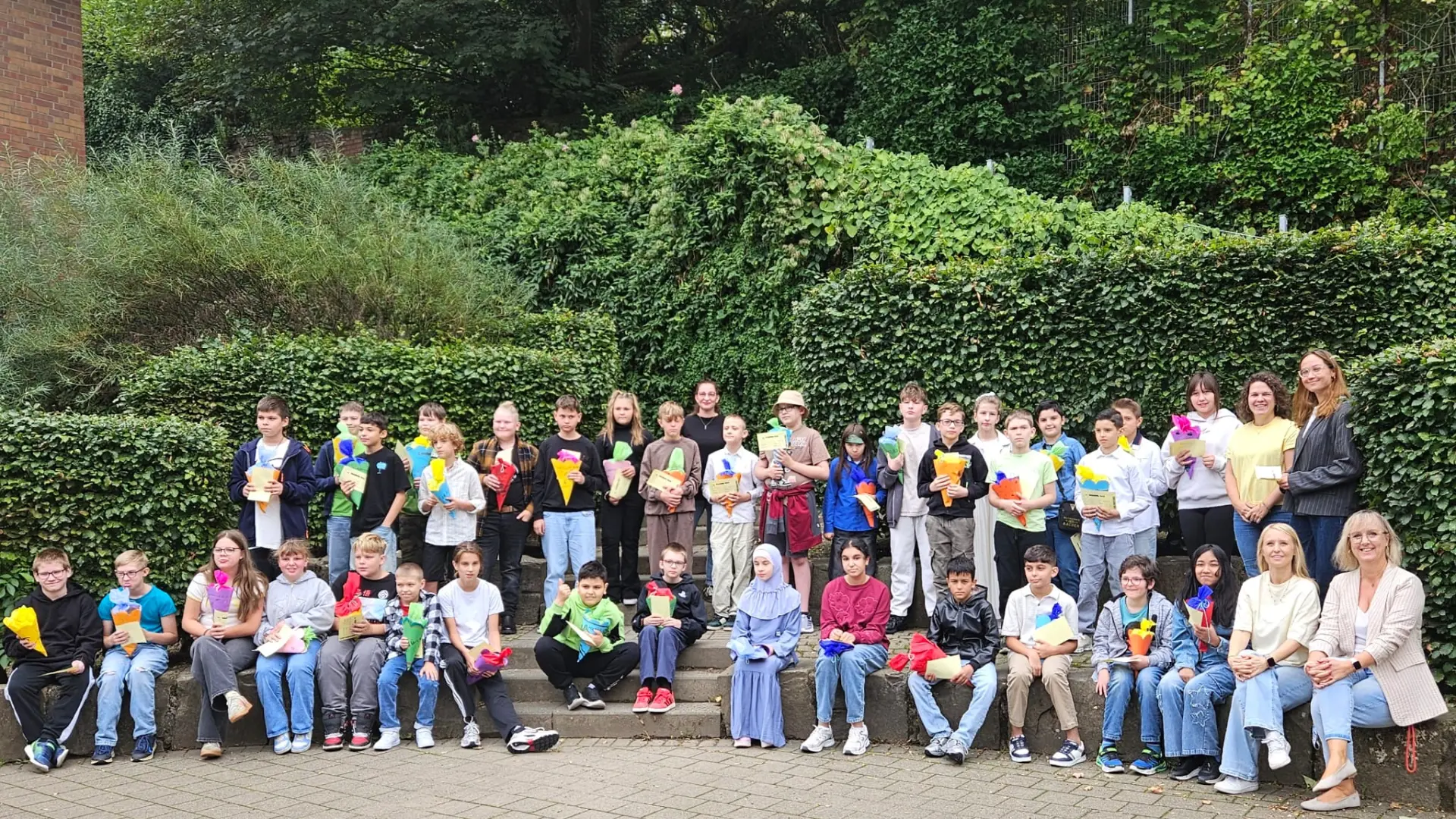 Auf der Bühne in der Schulaula sitzen fünf Schüler*innen. Sie werden von hinten aufgenommen, vor ihnen im vollen Saal sitzen viele weitere Schüler*innen und schauen sich die Diskussionsrunde an.