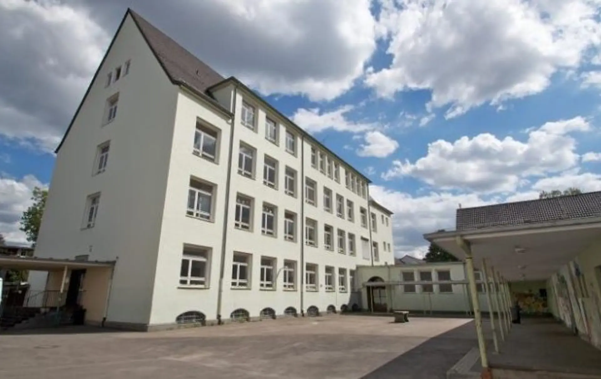 Außenansicht des historischen, hellen Schulgebäudes der LVR-Heinrich-Welsch-Schule in der Albermannstraße in Köln-Kalk unter blauem Himmel mit Wolken.