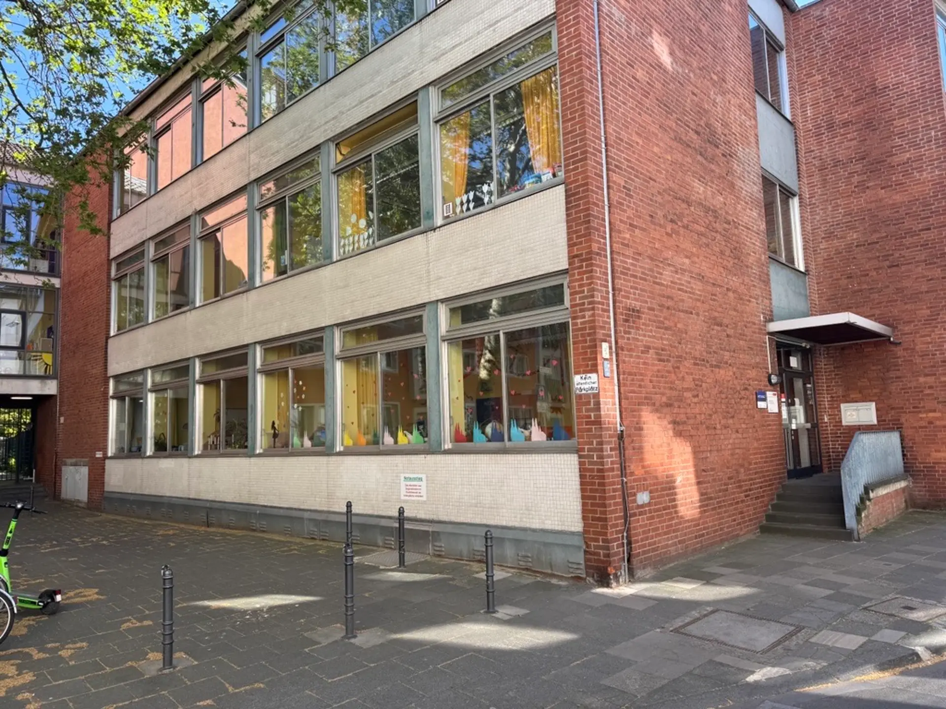 Außenansicht des Schulgebäudes am Marienplatz, ein mehrstöckiger Backsteinbau mit großen Fensterfronten und einem Eingangsbereich mit kleiner Treppe.