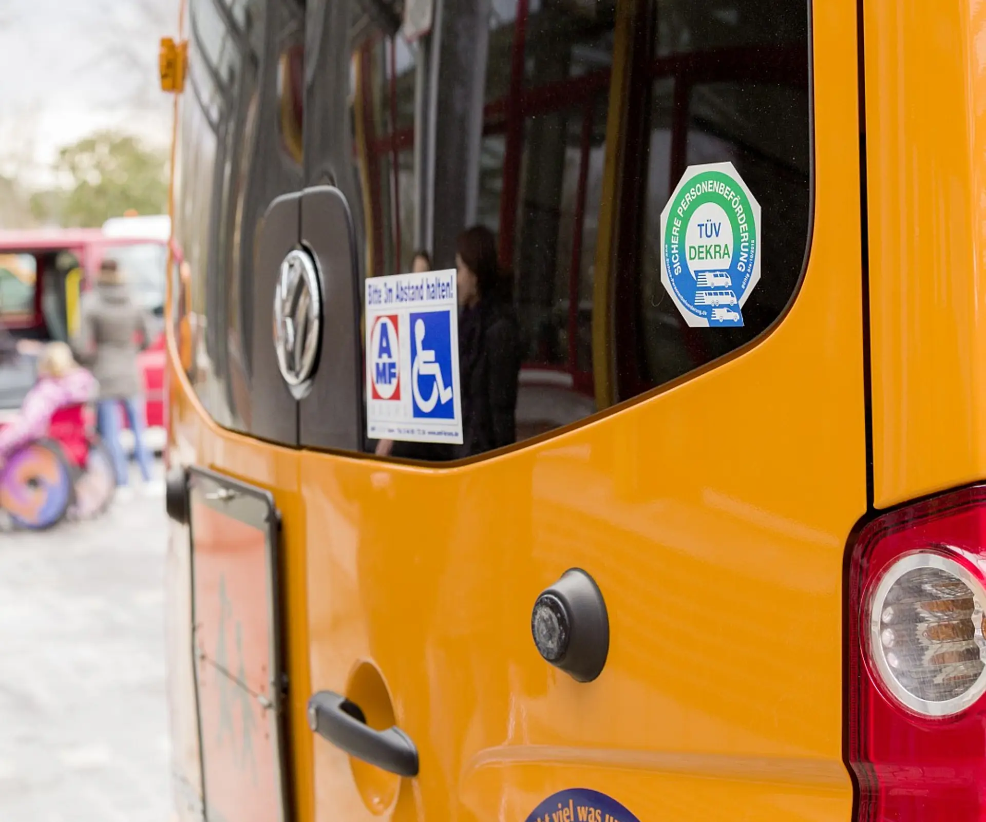 Die hintere Tür eines Fahrzeuges zur Beförderung von Menschen. An der Glasscheibe sind verschiede Aufkleber geklebt, darunter ein Zeichen für Menschen im Rollstuhl und ein TÜV-Prüfungssiegel.
