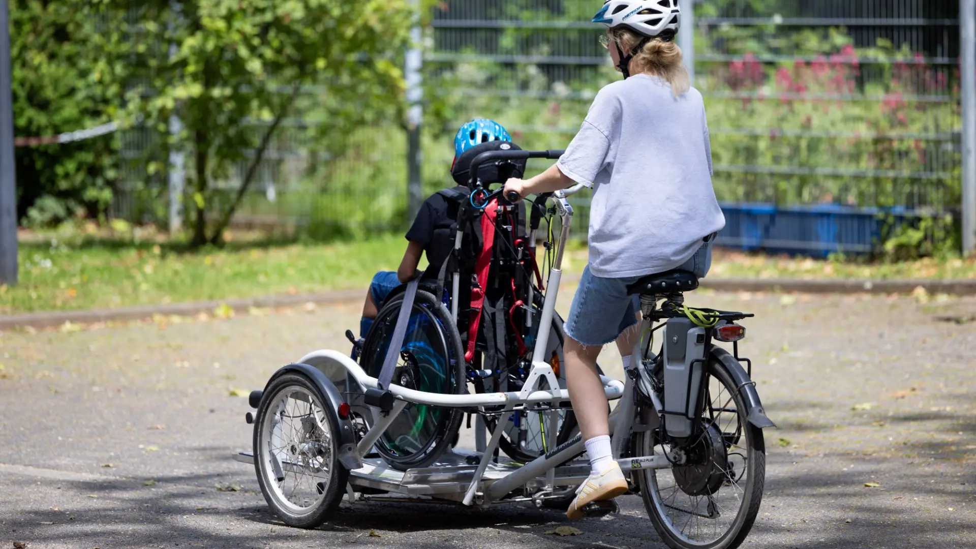 Eine erwachsene Person fährt auf einem speziellen E-Bike ein Schulkind samt seinem Rollstuhl.