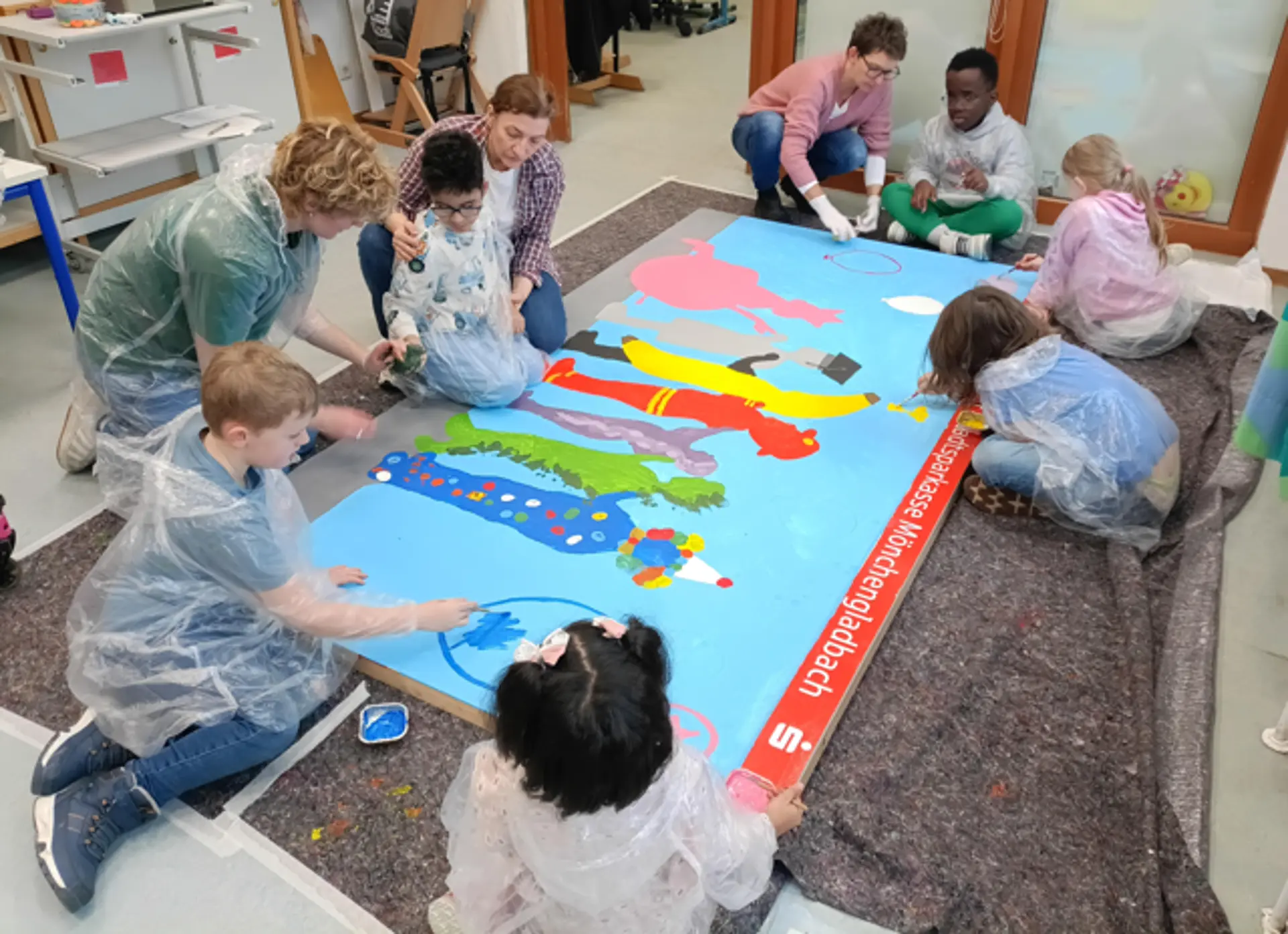 Erwachsene und Kinder malen Ballons aufm Bild mit den bunten Umrissen der Kinder.