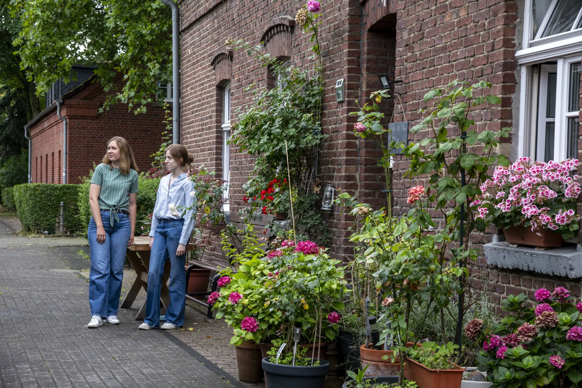 Zwei Frauen stehen vor einem Haus mit vielen Blumen im Vorgarten