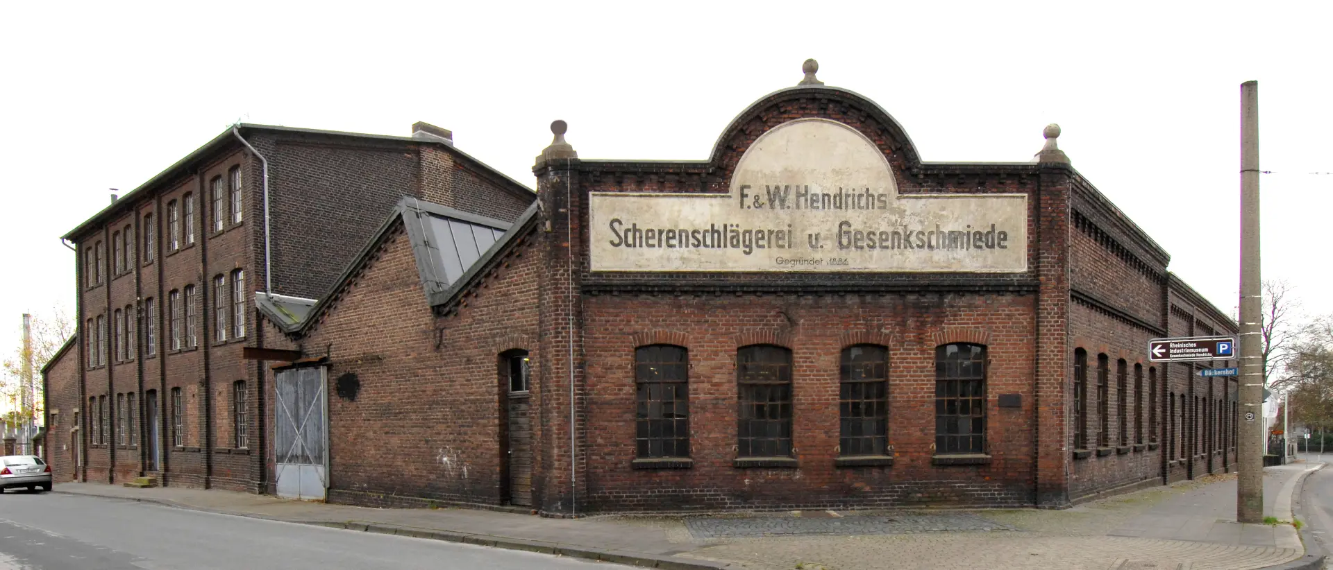 Ein Backsteingebäude an einer Straßenecke, auf dem ein Schild mit dem Namen "Gesenkschmiede Hendrichs" angebracht ist.