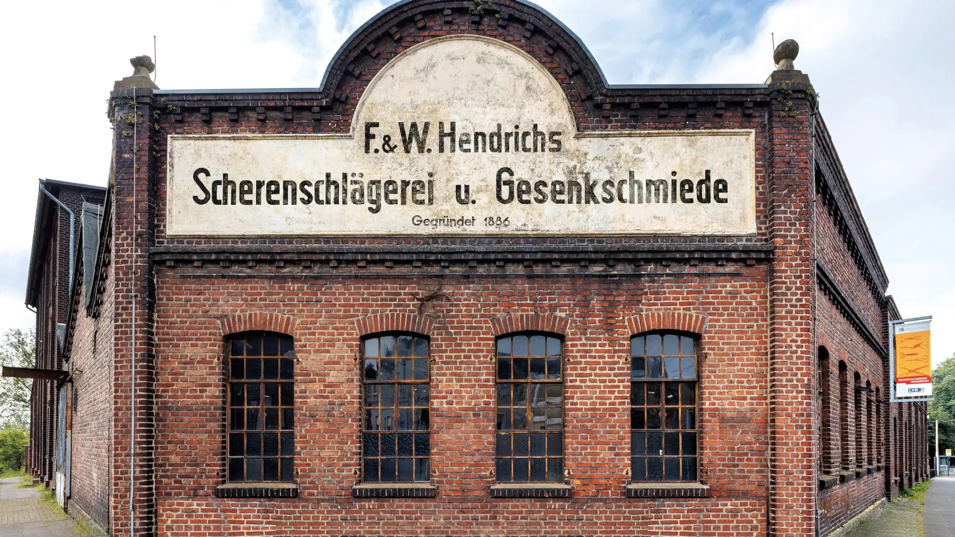 Ein rot-braunes Backsteingebäude mit einem großen Schild, auf dem "Scherenschlägerei und Gesenkschmiede" steht.