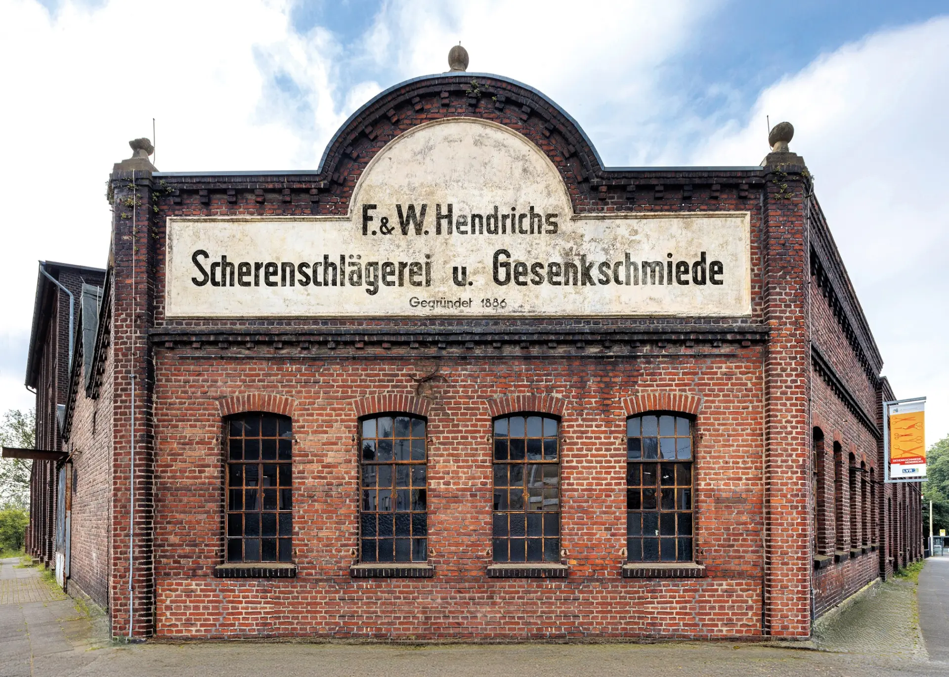 Ein rot-braunes Backsteingebäude mit einem großen Schild, auf dem "Scherenschlägerei und Gesenkschmiede" steht.
