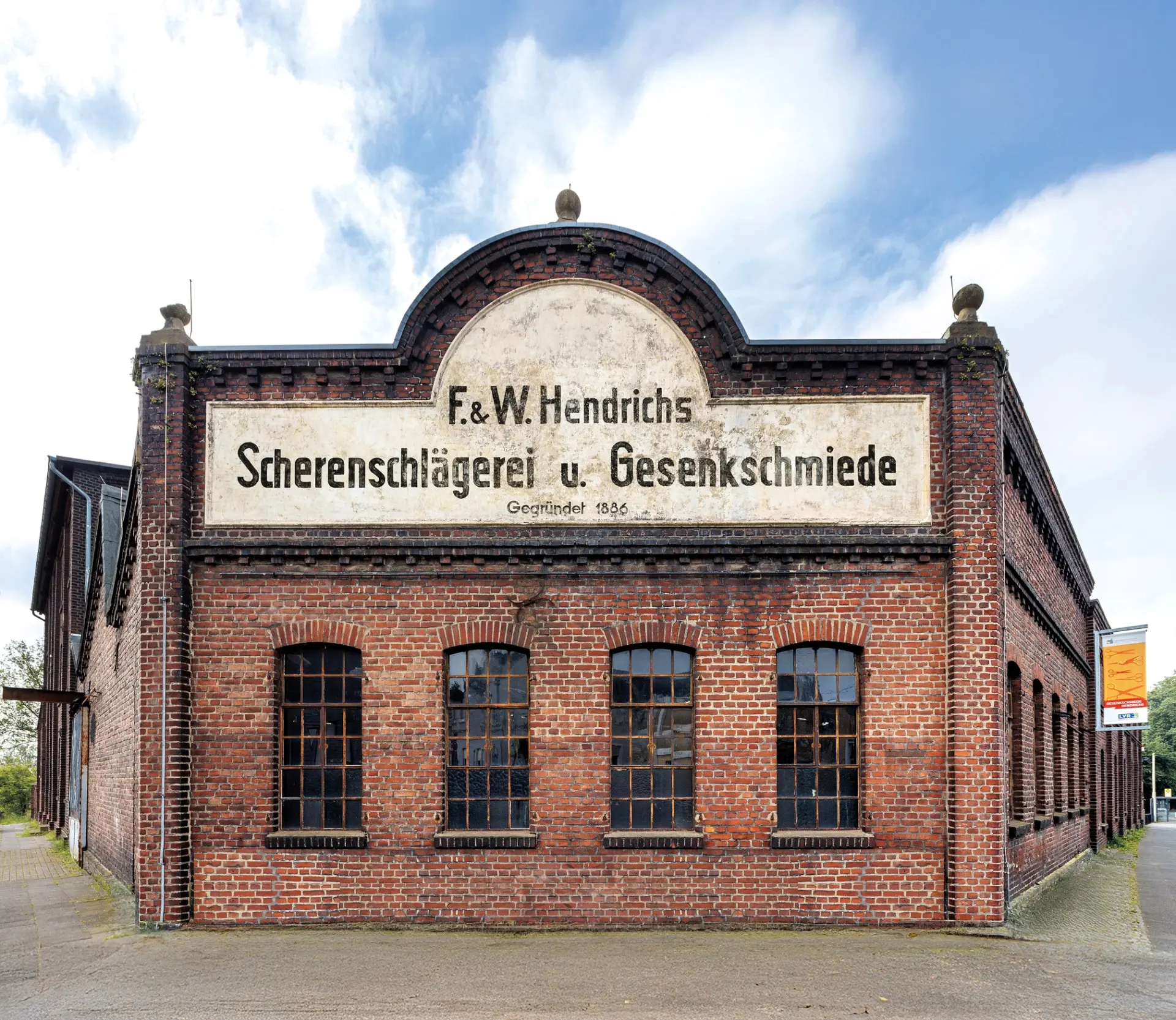 Ein rot-braunes Backsteingebäude mit einem großen Schild, auf dem "Scherenschlägerei und Gesenkschmiede" steht.