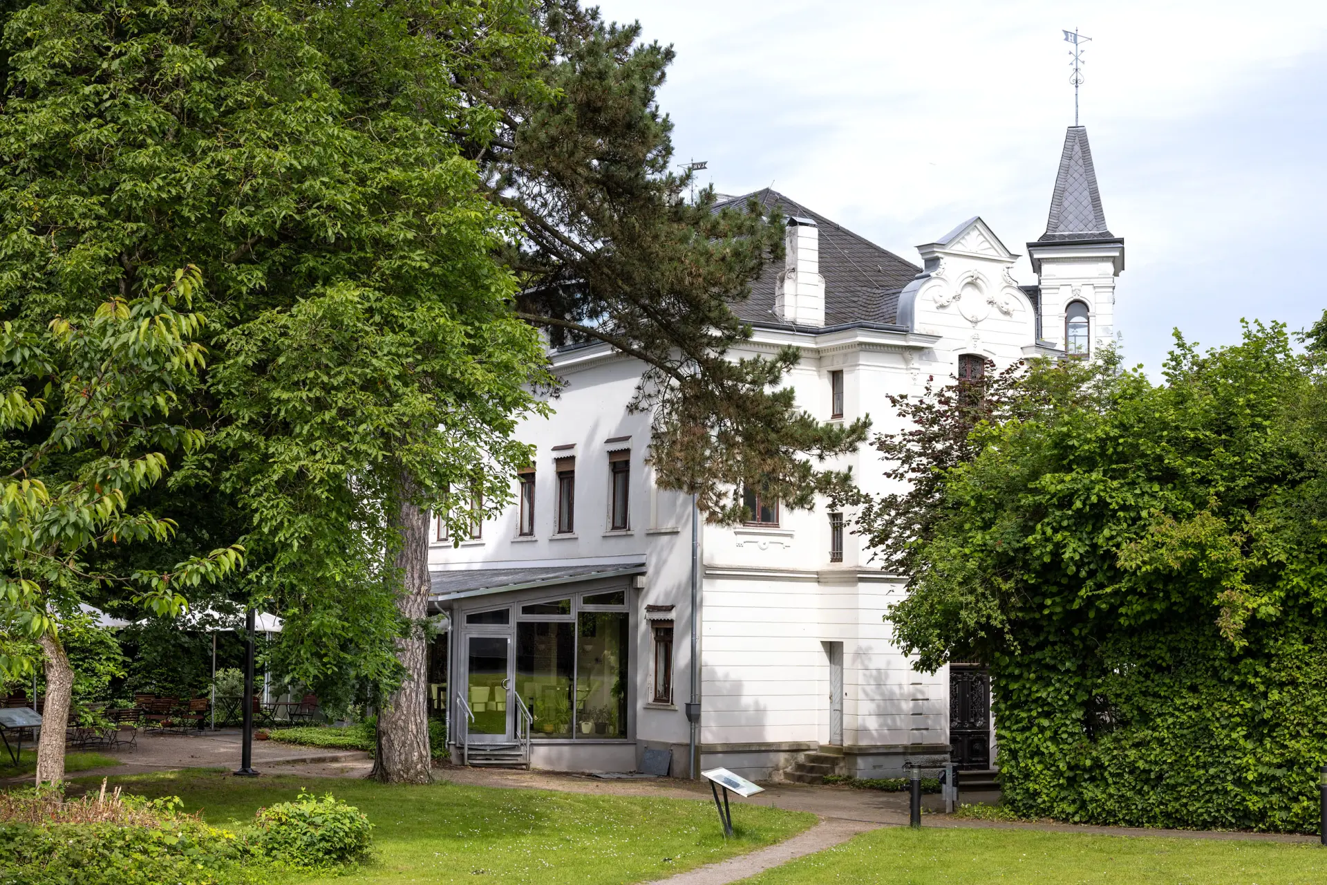 Eine weiße Villa zwischen grünen Bäumen.