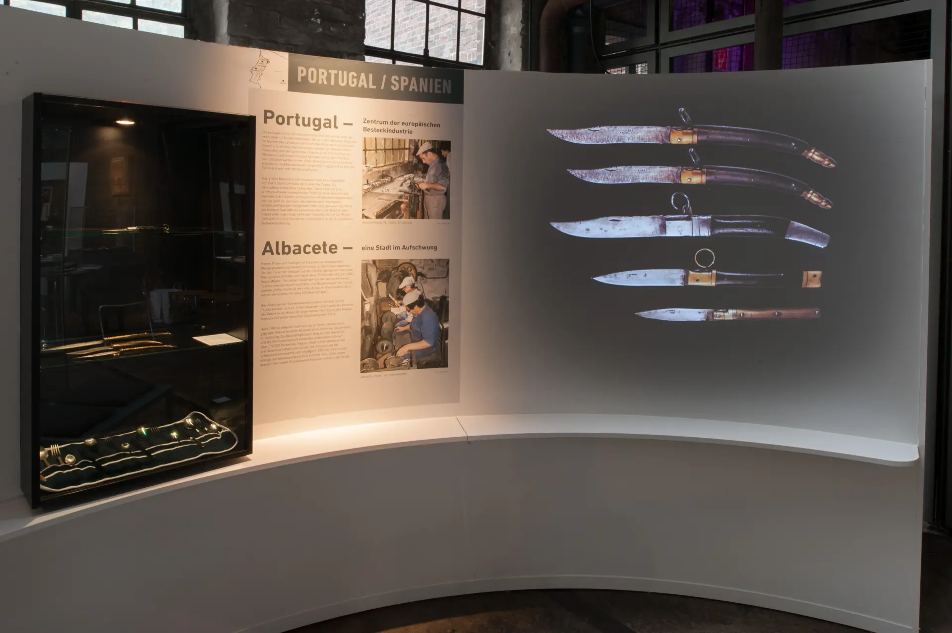 Blick auf eine Ausstellungsvitrine, in der Messer in verschiedenen Größen zu sehen sind. Daneben befinden sich Infotafeln.